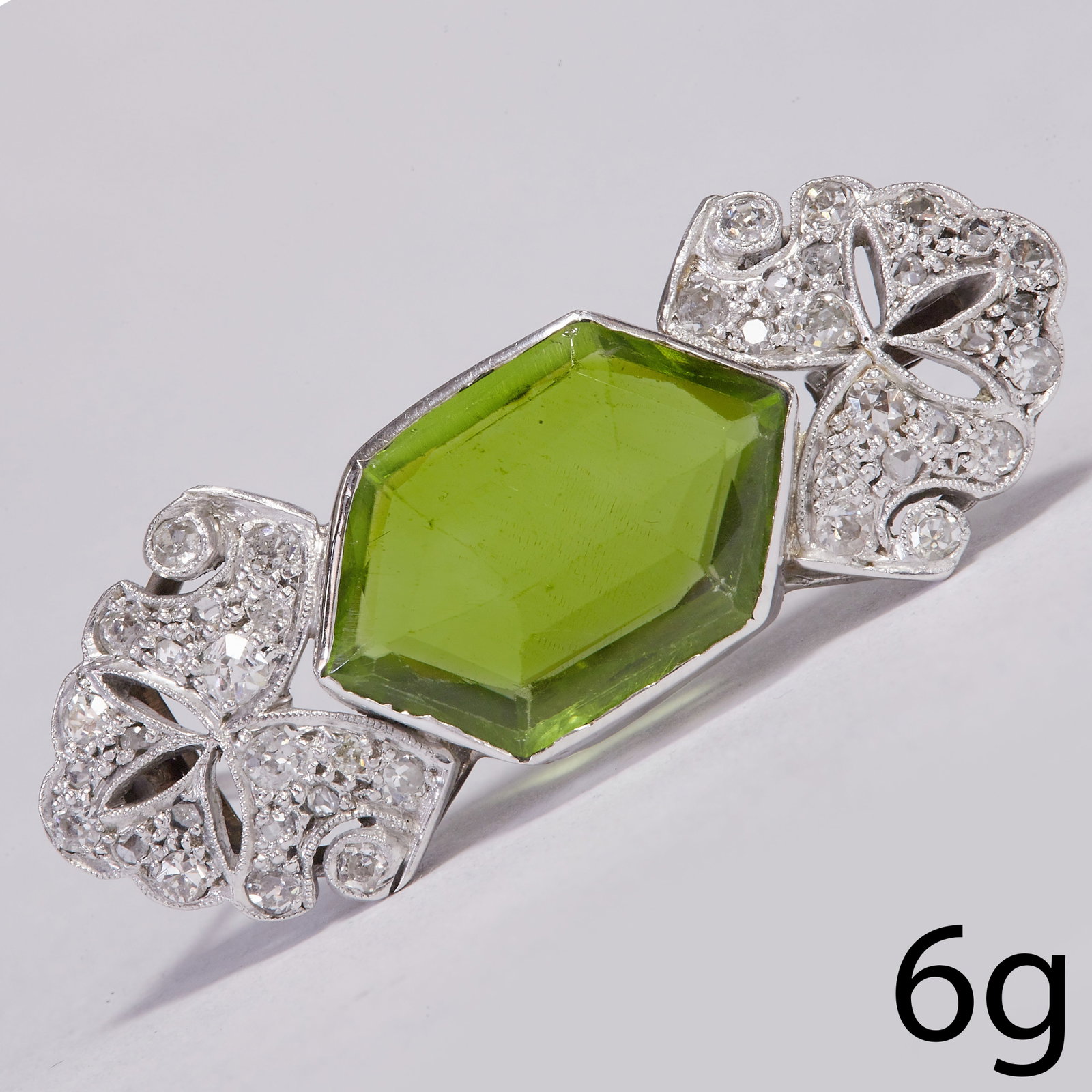ART-DECO PERIDOT AND DIAMOND BROOCH: ART-DECO PERIDOT AND DIAMOND BROOCH,Vibrant and rich coloured peridot of approx. 4.30 ct.Diamonds bright and lively, totaling approx. 0.50 ct.W. 3.6 cm.6 grams.