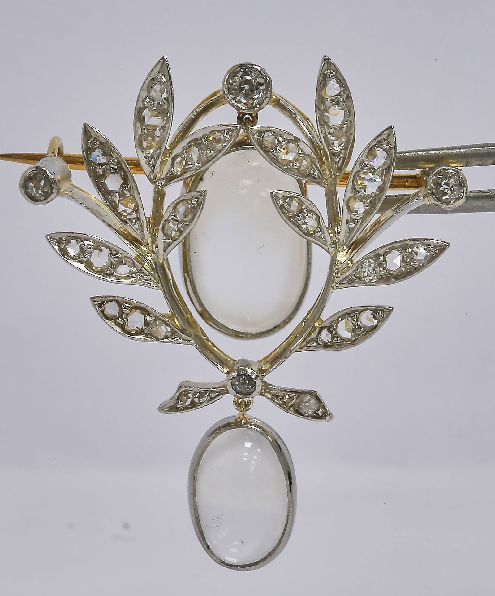 MOONSTONE AND DIAMOND BROOCH: MOONSTONE AND DIAMOND BROOCH,8.1 grams, testing high carat gold and platinum.Moonstones articulated, with blue shiller.L. 3,4 cm.