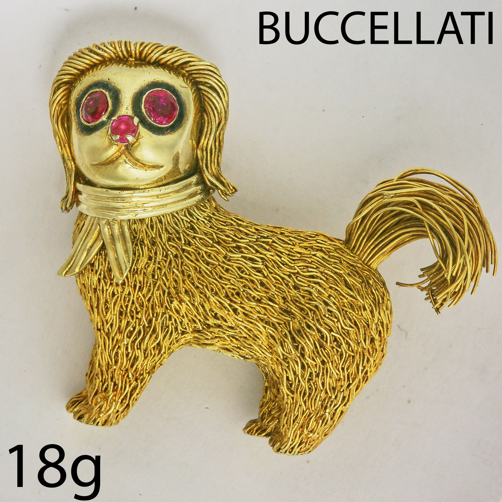 BUCCELLATI, RUBY AND ENAMEL DOG BROOCH: BUCCELLATI, RUBY AND ENAMEL DOG BROOCH,18 grams, 18 ct. gold.The dog of fine wire work design.They eyes and nose set with rubies, and enamel accents.Signed Buccellati.L. 4.5 cm.