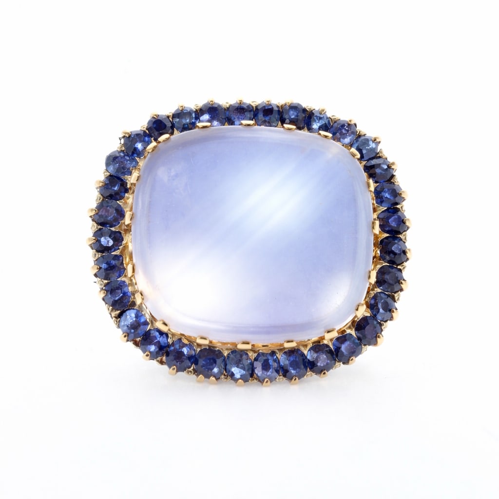 LARGE MOONSTONE AND SAPPHIRE GOLD BROOCH: LARGE MOONSTONE AND SAPPHIRE GOLD BROOCH,18 grams.Large moonstone with nice blue shiller of approx. 30 ct.Surrounded by rich and vibrant sapphires, totalling approx. 3.40 ct.W. 3.2 cm.