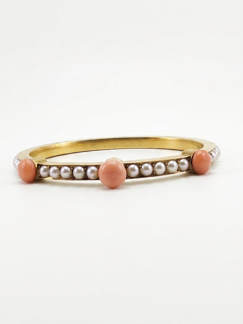 VICTORIAN PEARL AND CORAL HINGED BANGLE: VICTORIAN PEARL AND CORAL HINGED BANGLE,12.8 grams, testing 18 ct. gold.Lovely pearls, accentuated with 3 larger corals.Largest coral of approx. 7.2 mm.Inner diam. 5.6 cm.