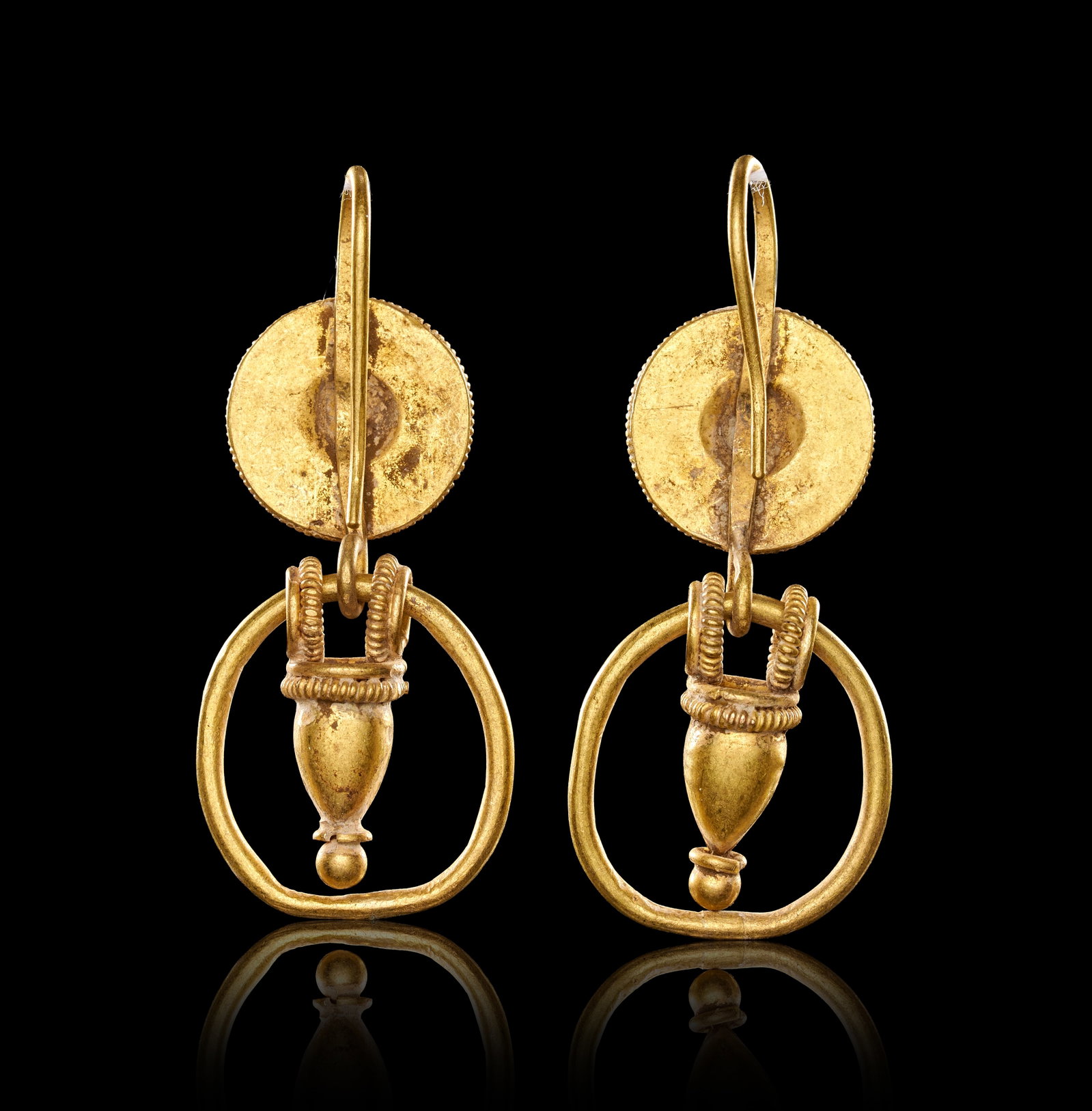 RARE PAIR OR ROMAN URN EARRINGS: RARE PAIR OR ROMAN URN EARRINGS,8.5 grams, testing high carat gold.By repute 1st-2nd century AD.The tops of disk shape with wire detailed borders.Suspending an articulated urn vase within a hoop.L. 4