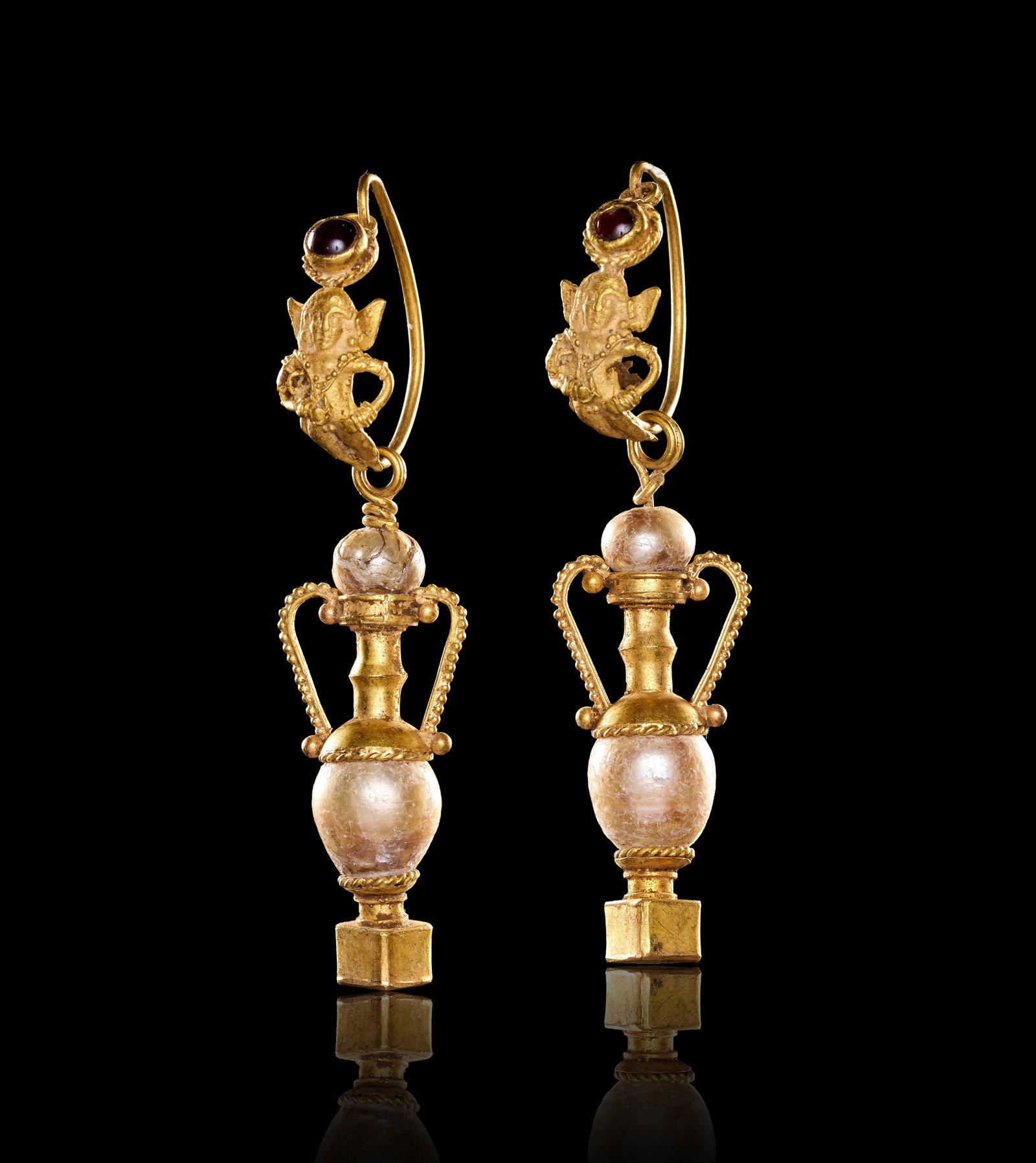 RARE PAIR OF HELLENISTIC GOLD AND GARNET EROS AND AMPHORA EARRINGS: RARE PAIR OF HELLENISTIC GOLD AND GARNET EROS AND AMPHORA EARRINGS,9.9 grams, testing high carat gold.By repute 2nd century BC.The tops in fine relief decoration depicting Eros, topped with a
