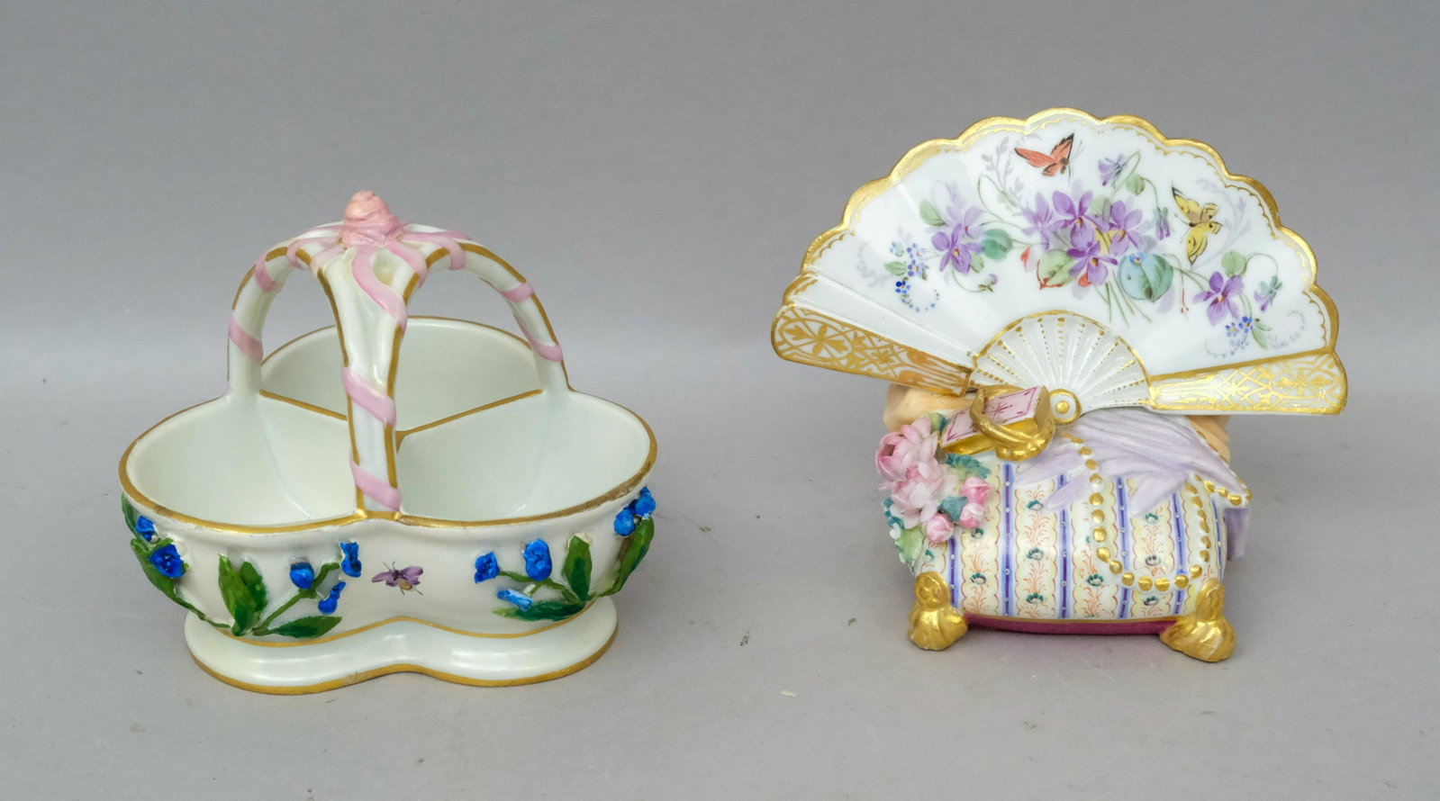 2 Pieces of Meissen Porcelain: Comprising a basket with applied flowers, and a hand fan form place card holder decorated with butterflies. Basket 4" across and the holder 4" tall.