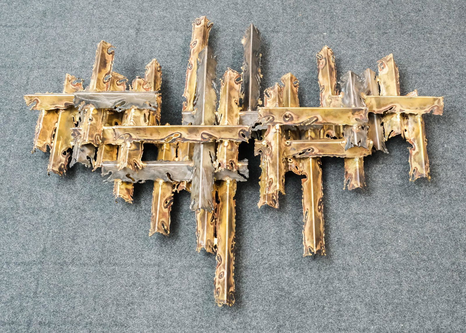 Tom Greene, MCM Wall Mounted Sculpture: Tom Greene (American, 1942-2012), mid-century, brutalist metal wall mounted sculpture made up of criss-crossing strips of fire-cut metal, 36" x 48" overall.