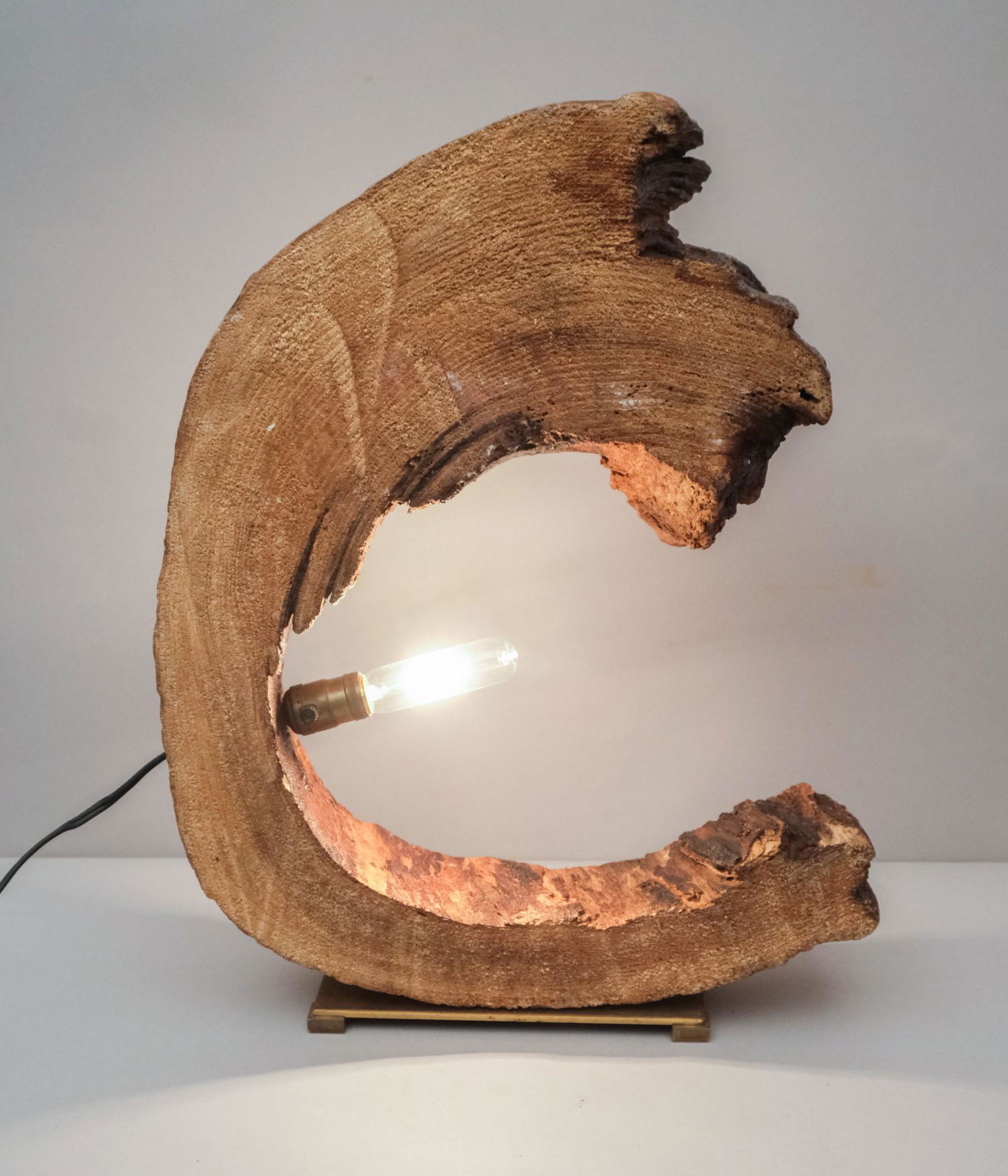 Hollow Trunk Crescent-Shaped Lamp: Mid-century lamp made from a hollowed slab of wood, the rough edges glazed over to prevent slivers, in the shape of a crescent, mounted on a brass stand, signed "Frank Stieger, Newton Highlands, Mass.