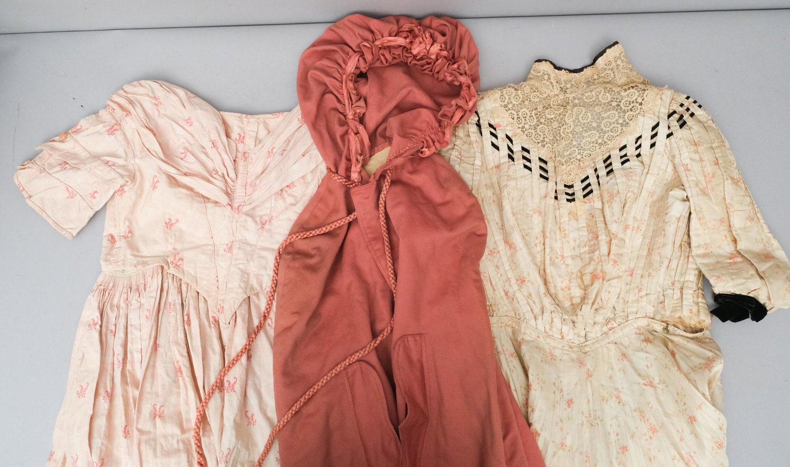 Lot of Edwardian Clothing: Lot consisting of a small sized, silky, handmade prairie-style dress with lace and interwoven ribbons at the throat with clasp closures; a pink, handmade Edwardian dress with clasp closures up the bac