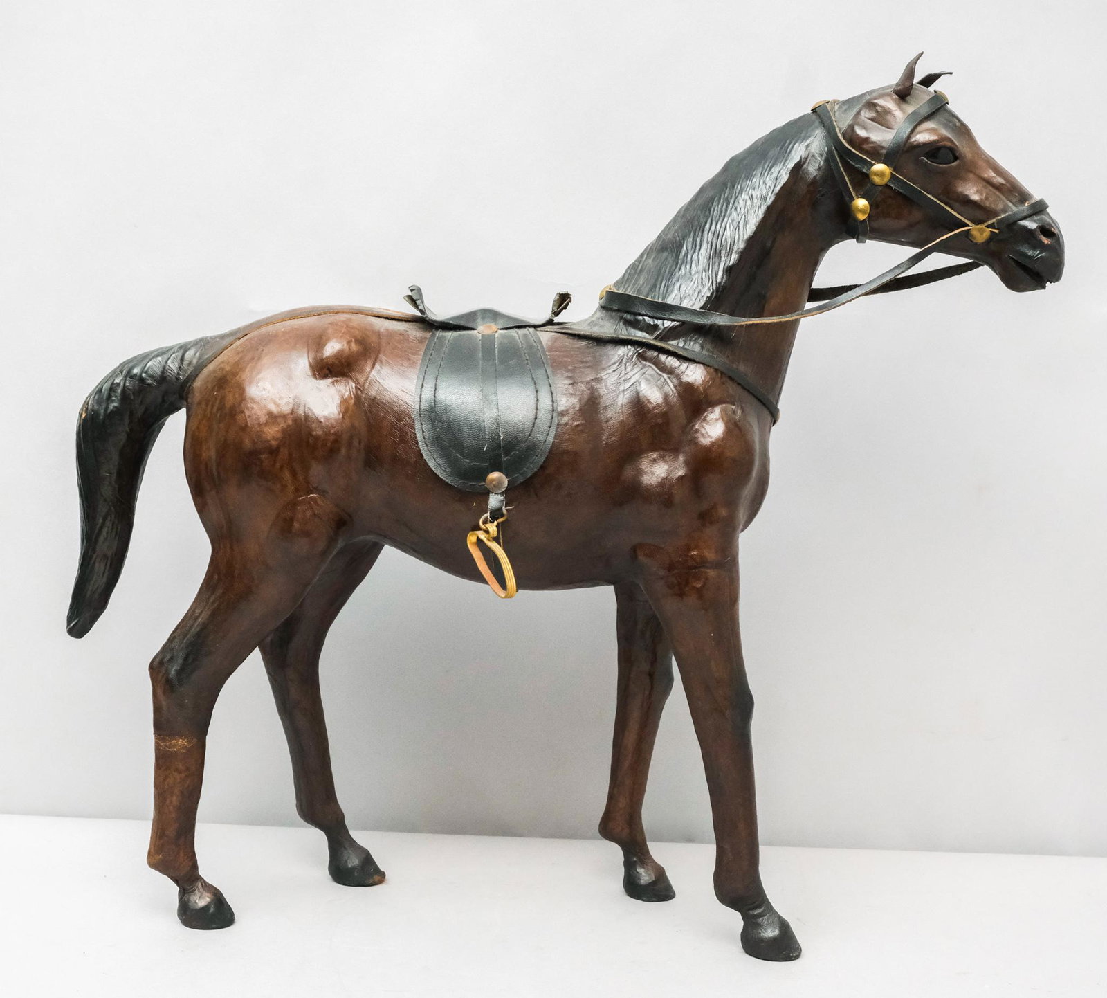 Wood & Brown Leather Horse Figurine: American, late 19th century wooden horse figurine covered in stretched brown leather, leather harness with brass hardware, glass eyes, 19" H x 6" W x 21" L.