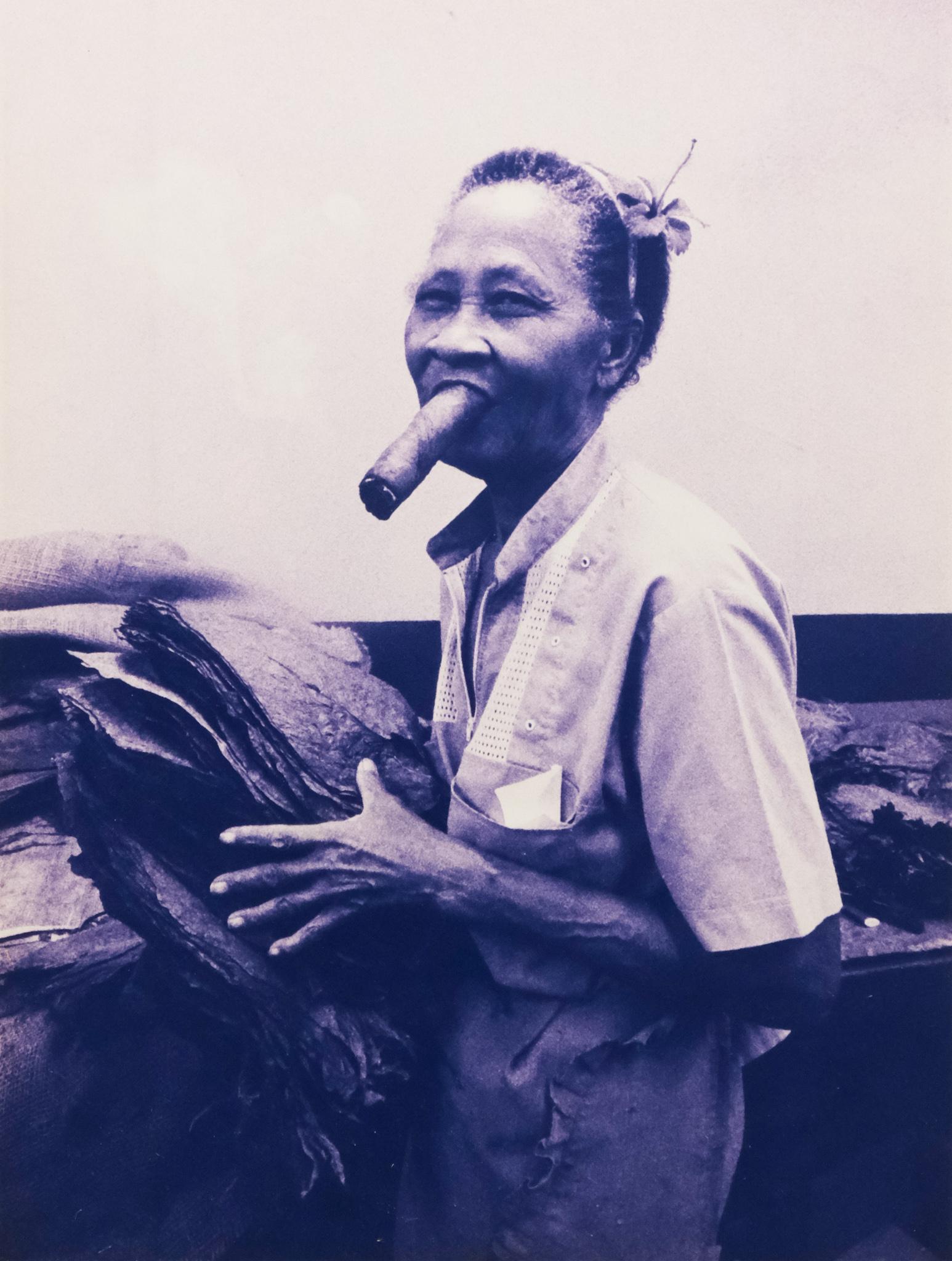 Vintage Photo of Cigar Factory Worker: 1997 photograph of a woman with a large cigar between her teeth, working at a cigar factory in Cuba, signed and dated l.l., 11 3/4" x 15 3/4" print, 17 1/4" x 21" framed.