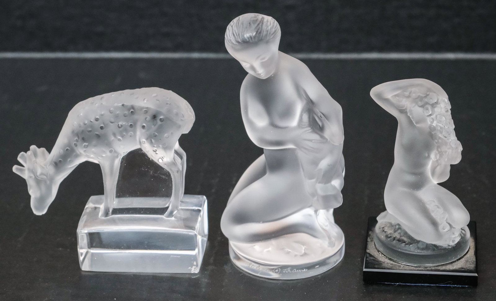 Lot of Lalique Crystal Glass Figurines Paperweight: Comprising a nude kneeling with a rabbit, another with flowers, and a deer. Marked as shown. Largest measures 2 1/2" width X 2 1/2" depth X 4 1/2" height.