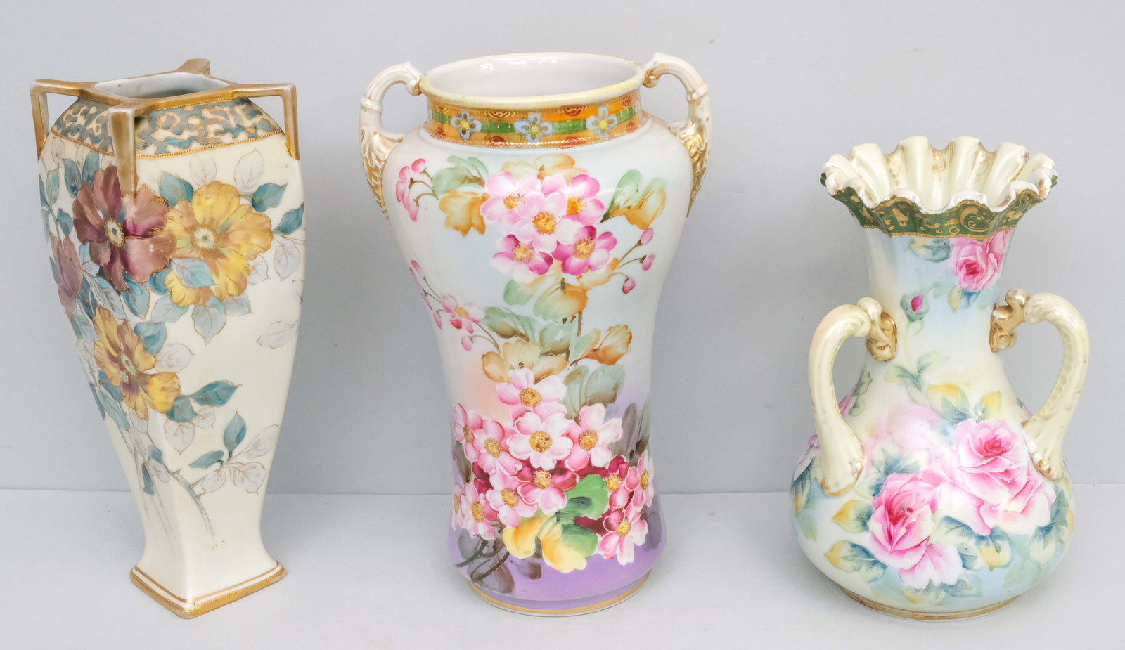 Three Antique Nippon Porcelain Vases: Comprising a Morimura Gumi vase with ruffled rim and loop handles (small flake to underside of top rim), a squarish example with small angular handles by Morimura, and another hand painted Nippon vase