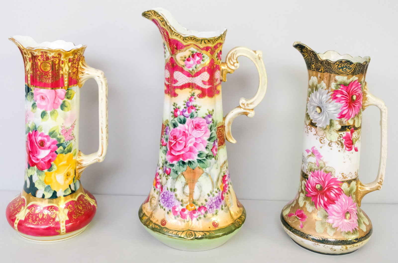 Three Antique Nippon Porcelain Pitchers: Comprising an unmarked Moriage pitcher, an Okan pitcher with green trim, and another unmarked example. 13" to 15".