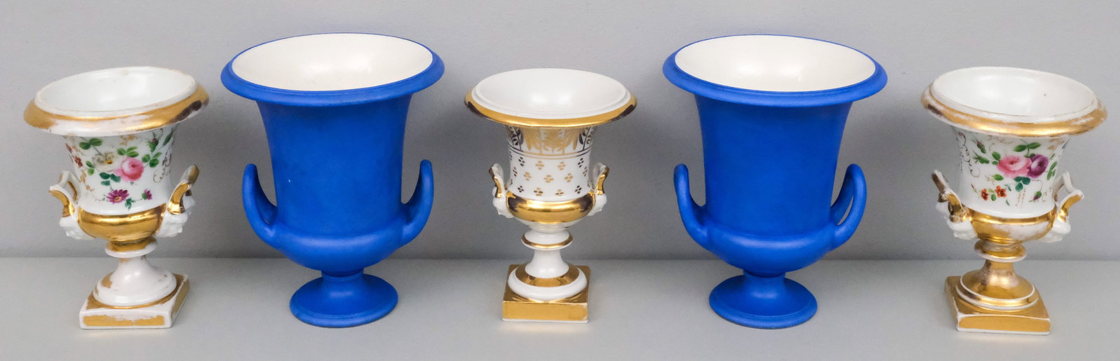 5 Antique Porcelain Garniture or Campagna Vases: Comprising a pair of Old Paris decorated with masks and flowers, an odd urn, and a pair of wedgwood urns with later blue paint.