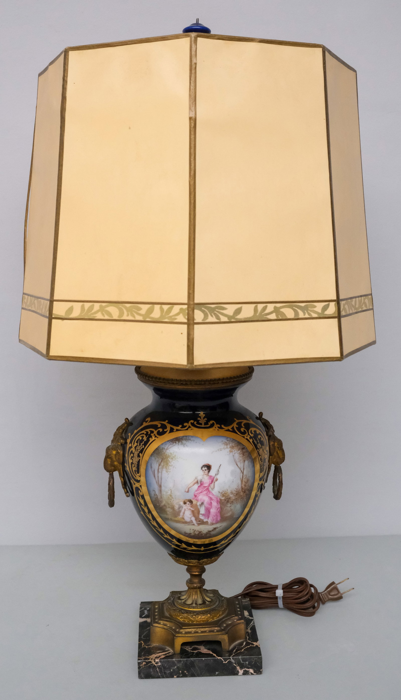 Sevres Porcelain Lamp: With brass rams head handles and romantic cartouche and decorated shade. 26". Together with lid (broken) bears Sevres mark.