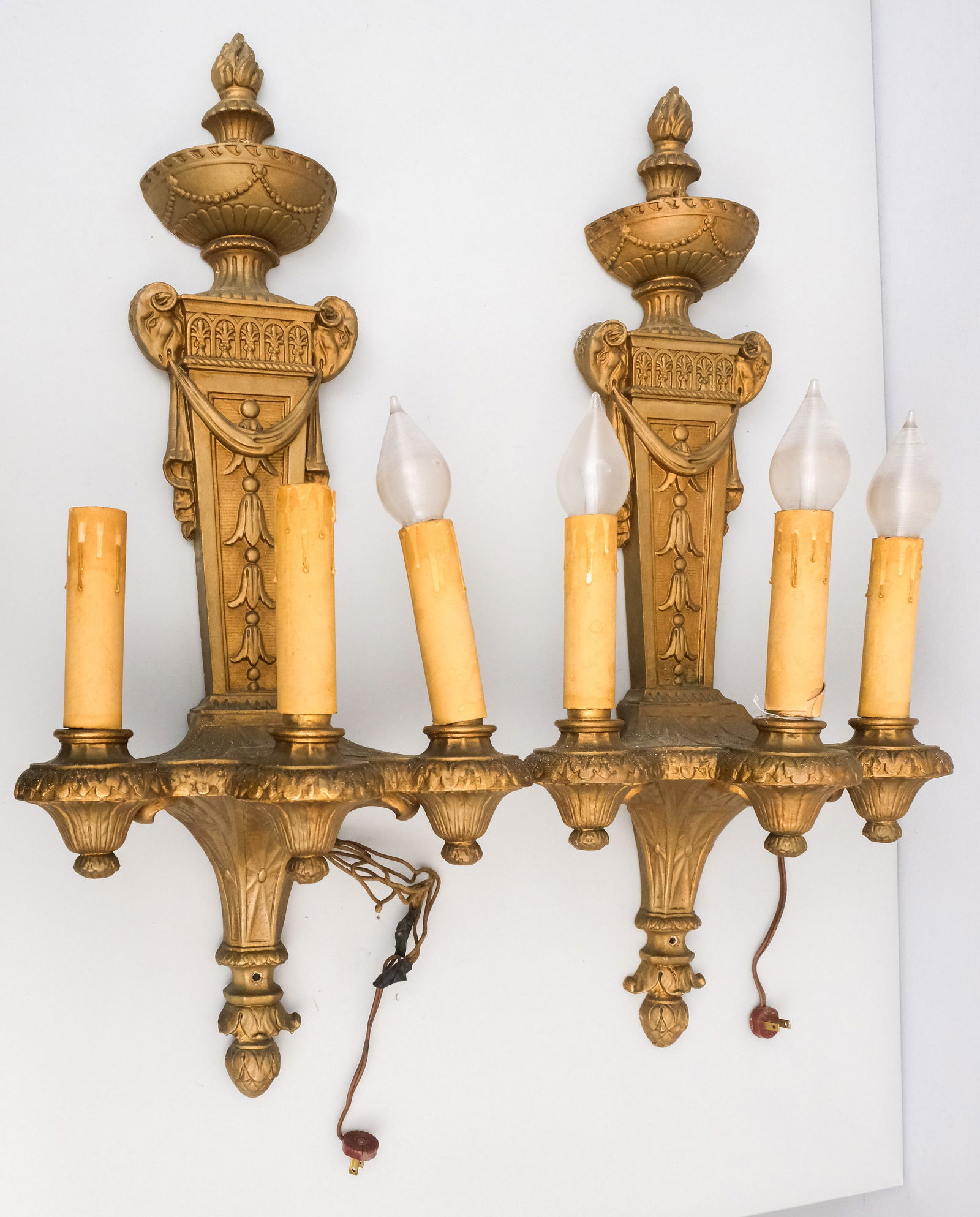 Pair Adams Style Three-Light Wall Sconces: Composite cast candelabra-type, with rams head decor and faux candlestick sockets. 13" x 31".