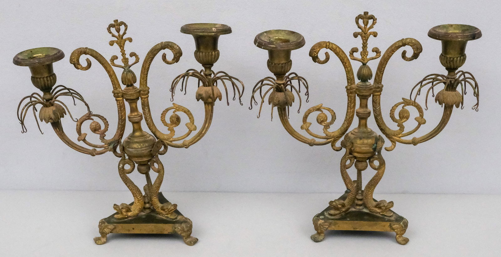 Pair of Antique Regency Candlesticks: Pair of late 19th century Regency style candlesticks, each with two candle holders, on a base of three dolphin forms, 10 3/4" H x 10" W x 4" L.
