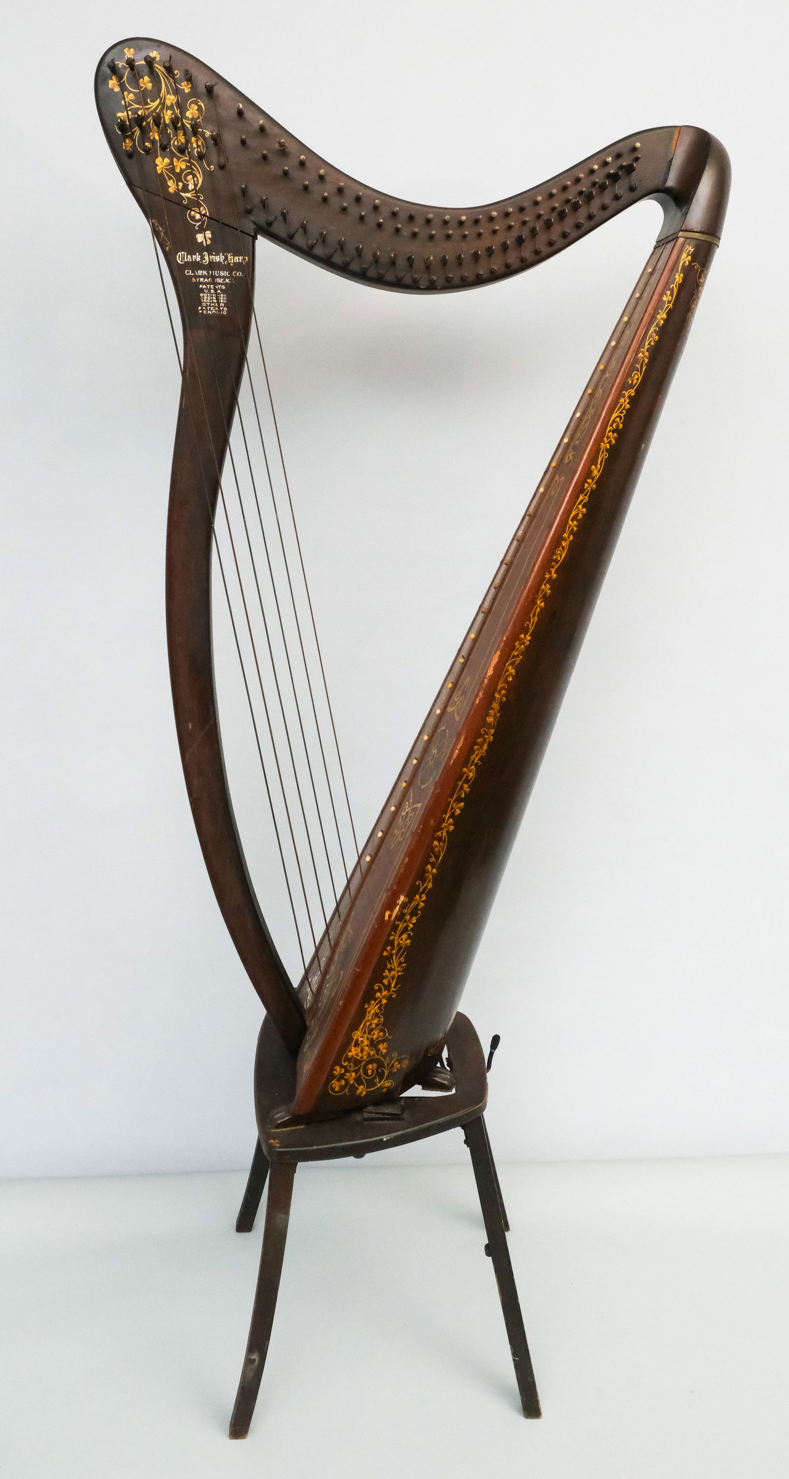 Antique Clark Irish Harp: Early 20th century Clark Irish Manufacturing Co., Syracuse, NY, harp with paw foot resting on a small black stand, decorated with Celtic knot designs, 53" H x 26" W x 13 1/2" L.