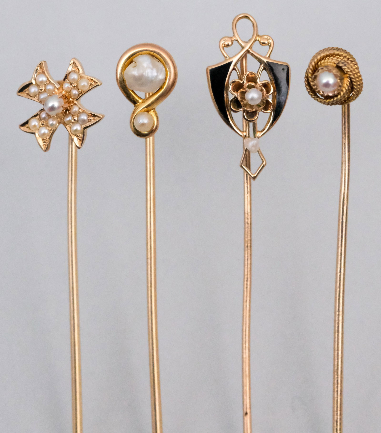 Group of Antique 10K & 14K Gold Stickpins: Victorian Era. Comprising a 14K knot with pearl, a 10K pearl and black enamel, a Baroque pearl, and a seed pearl Maltese cross. Weight of 14K 2.58 dwt, 10K 0.64 dwt.