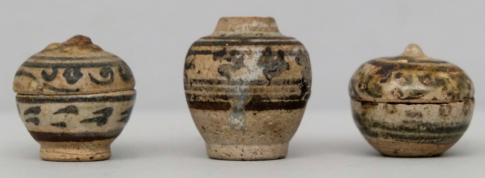 Three Miniature Sawankhalok ThaI Pottery Vessels: 18th Century or earlier. Comprising two lidded jars and a vase, all decorated with hand painted pattering. Delightful antique. 1 1/2" , 1 1/4", 1 1/4"