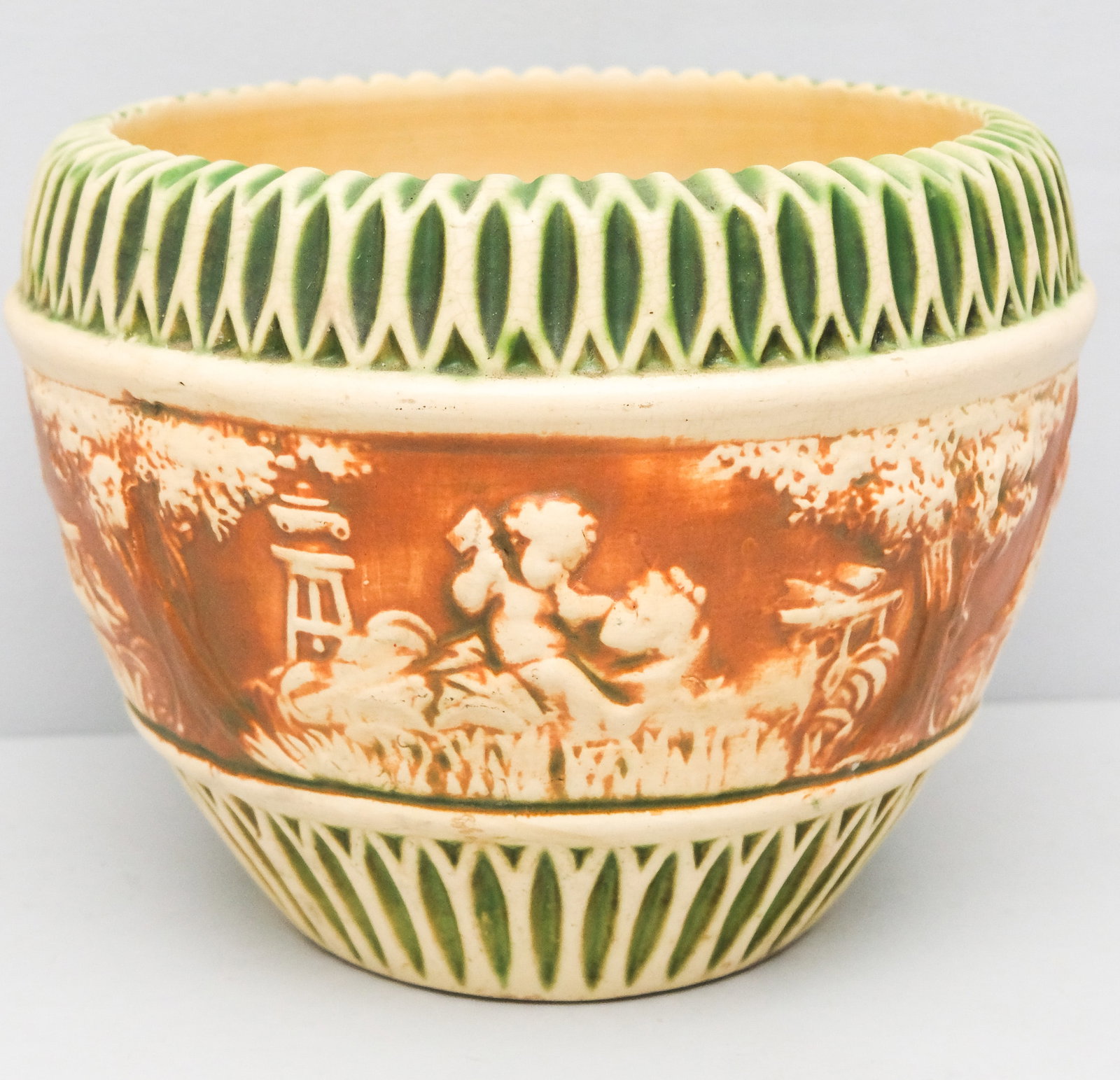 Roseville Donatello Art Pottery Jardiniere: Ribbed body with vertical green rib striping and putti decor. Unmarked. 9 1/2" x 13 1/2".
