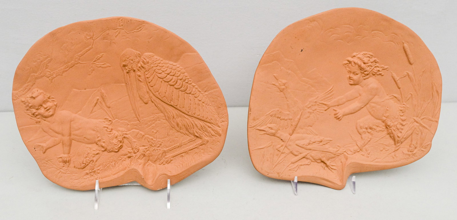 Two Ernst Wahliss Terracotta Plaques: Decorated with complimentary scenes of a young satyr frolicking with storks. Each 11".