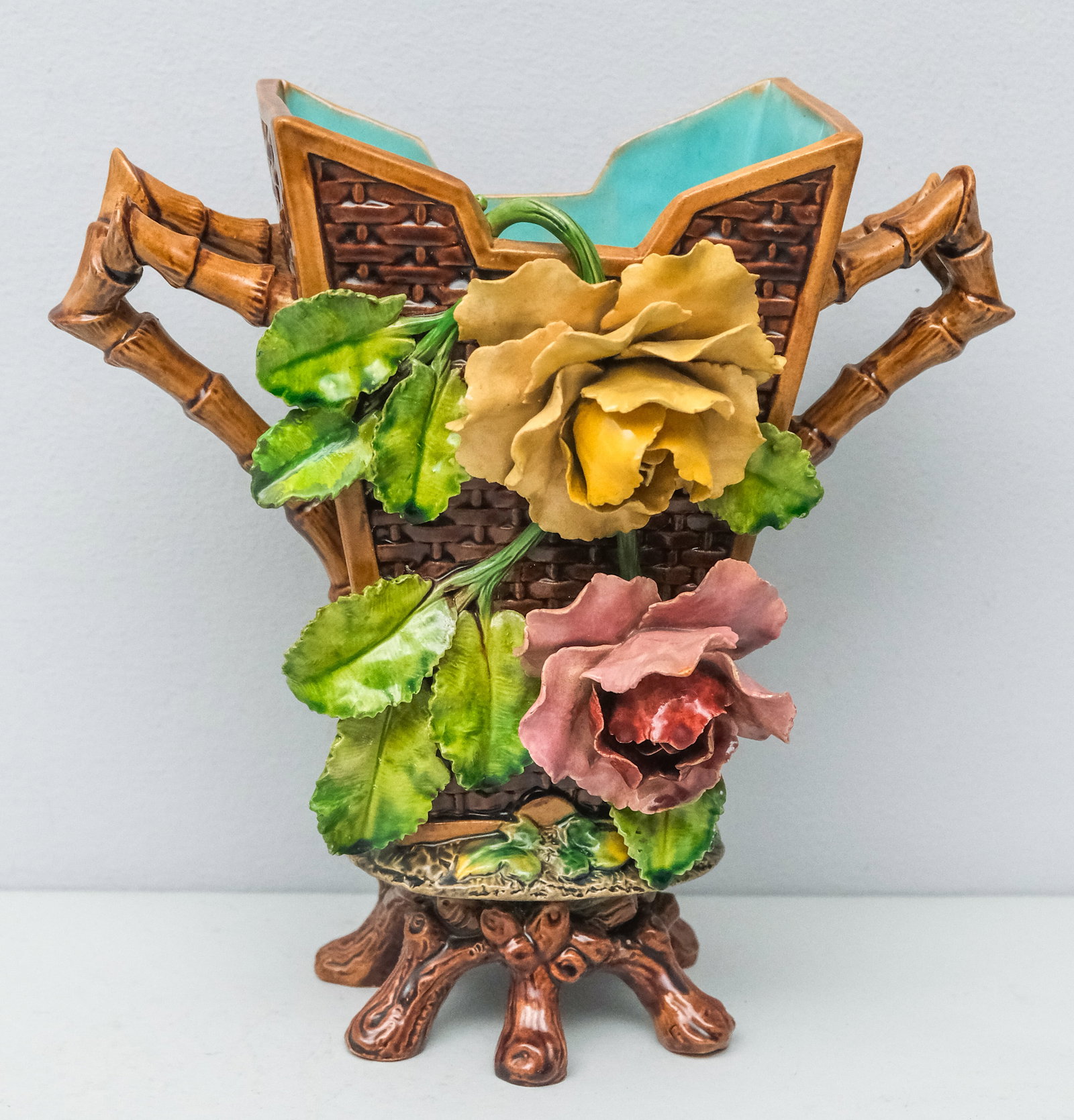 Wilhelm Schiller Majolica Orientalist Vase: Basket weave body with applied florals and bamboo handles, on faux bois base. 9 7/8".