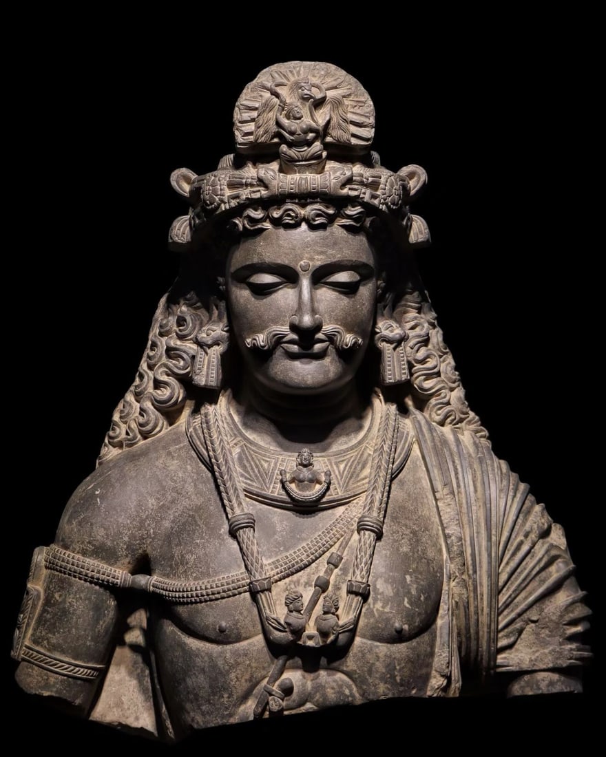 A 3TH-CENTURY GANDHARA BUST: Name A 3TH-CENTURY GANDHARA BUST Dimensions H:70cm This is a half-length grey sandstone figure in Gandhara style, with a round face and curly beard. It wears a precious crown decorated with Buddha's t