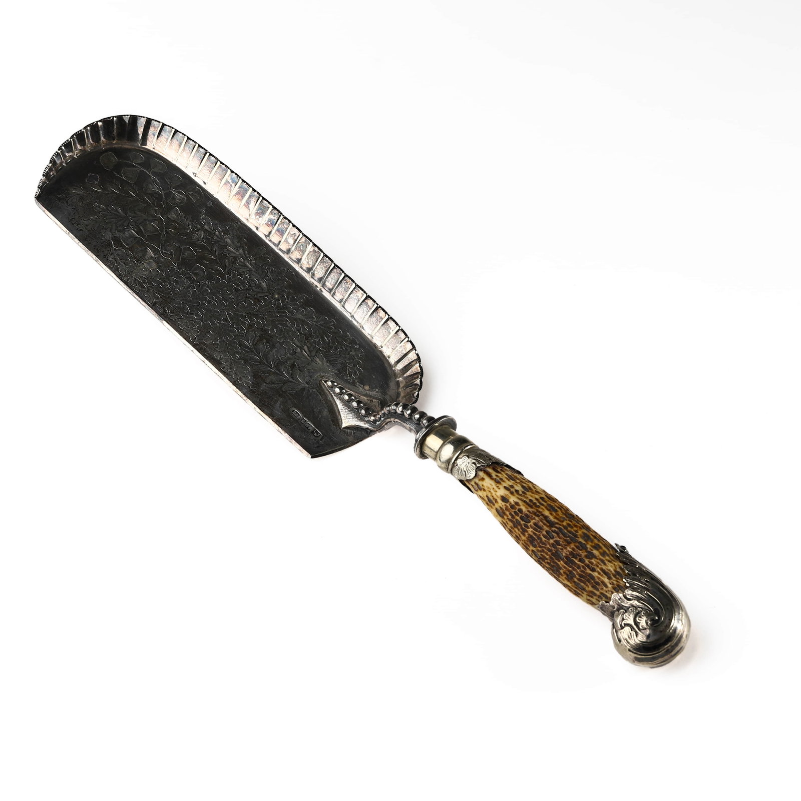 ANTLER-HANDLED ENGLISH SILVER CAKE SERVER: Length: 13 in. (33 cm), Weight: 2.9 oz. (82.1 g) This is a finely crafted English silver cake server featuring a richly decorated blade and a natural antler handle. The silver blade is embossed with a