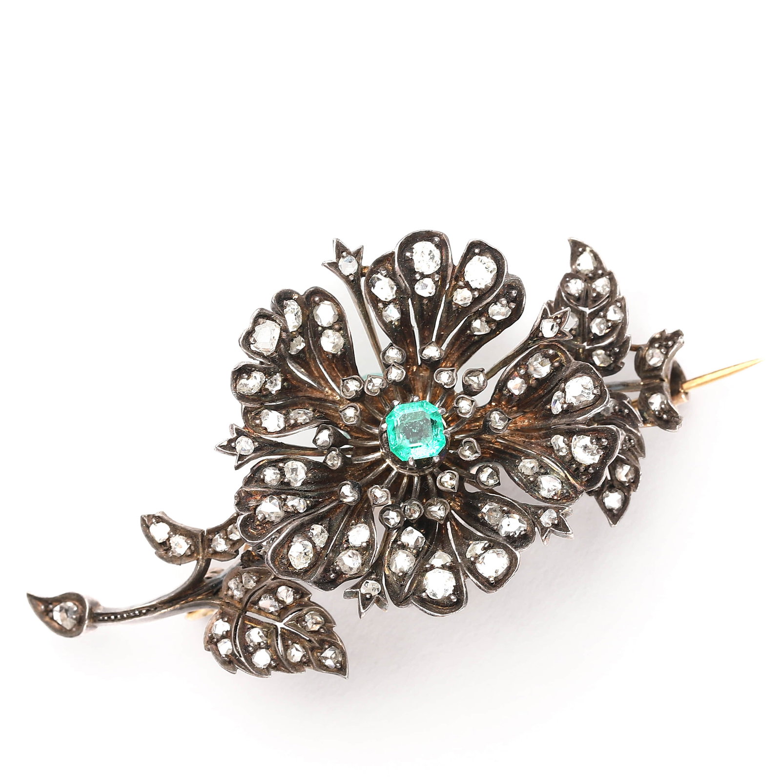 ANTIQUE SILVER-TOPPED GOLD, EMERALD AND DIAMOND BROOCH IN FLORAL FORM: Dimensions: Length: 3 1/16 in. (7.8 cm) Weight: Approx. 30 g Description: A striking antique brooch designed as a stylized flower, set with old rose-cut diamonds throughout and featuring a vivid green