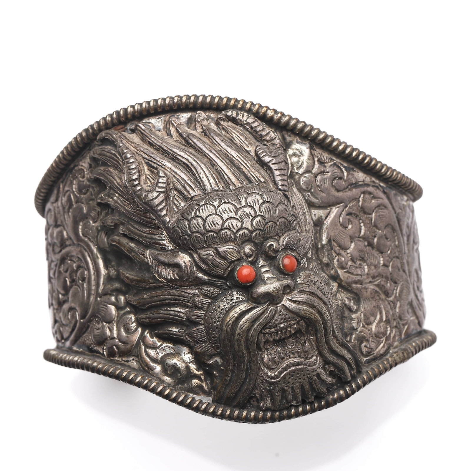 A SILVER DRAGON BRACELET: Dimensions Length: 3 1/8 in (8 cm)Weight: 107 g Description The wide cuff bracelet is richly repousse and chased with scrolling motifs and centered with a dramatic dragon mask in high relief, its fier