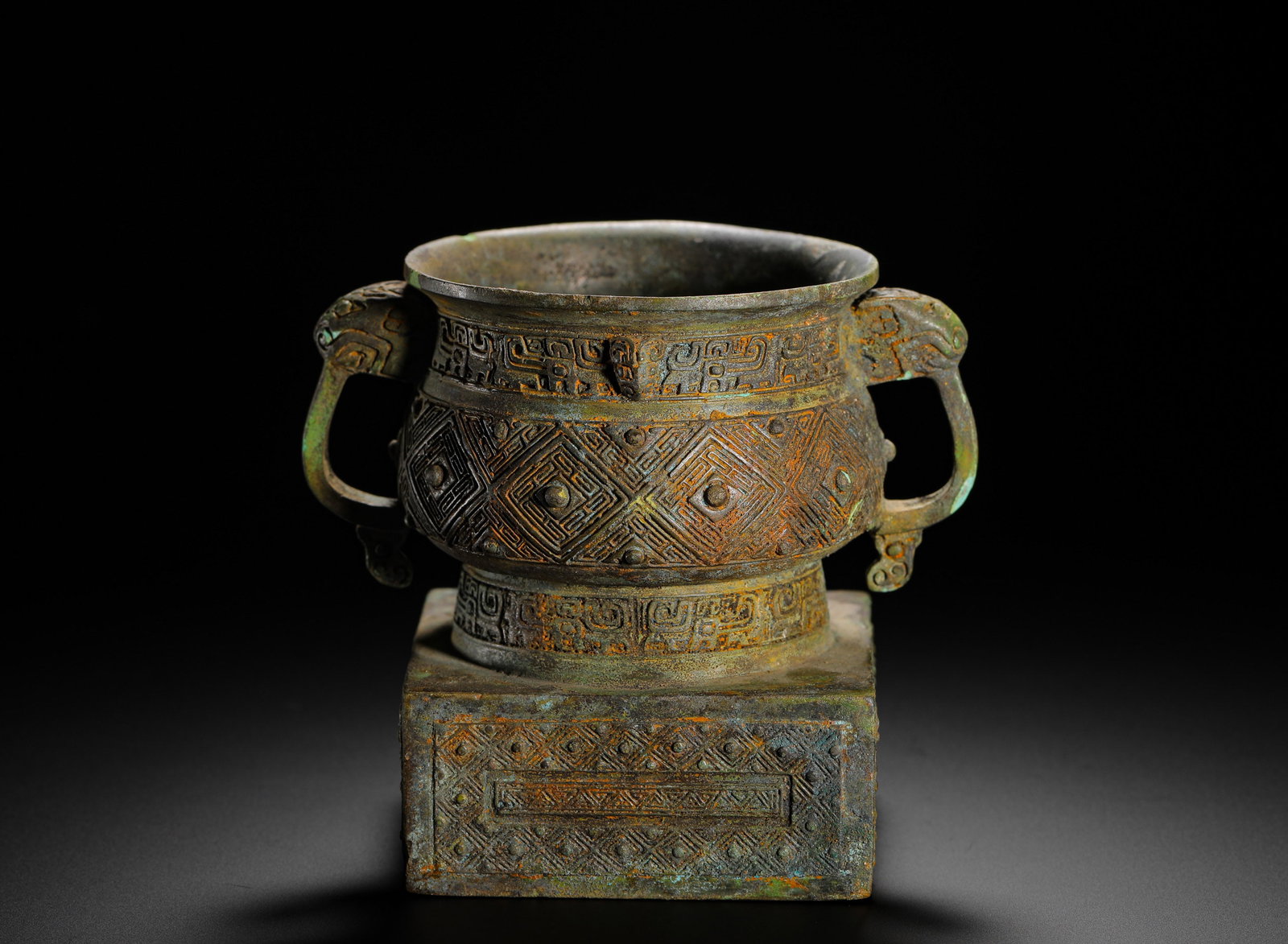 BRONZE THUNDER PATTERN SQUARE SEAT GUI FROM THE WESTERN ZHOU PERIOD: H:10cmW:12cmWeight:470g This is a Western Zhou Dynasty bronze ritual vessel. The body and square base are decorated with thunder and beast-face patterns, with beast-head handles on both sides. It is a