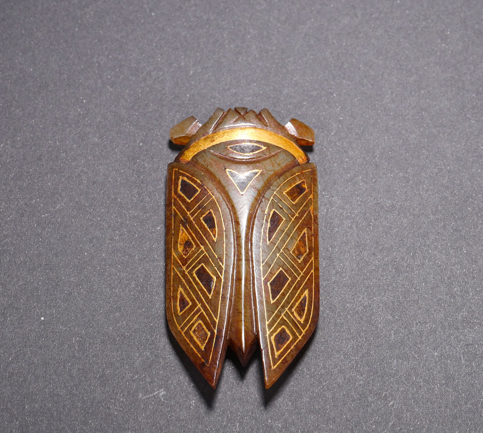 HAN DYNASTY HETIAN JADE GILDED GEOMETRIC PATTERN CICADA-SHAPED PENDANT: H:6.2cm(2.44in) W:3.1cm(1.22in) Weight:28g(0.06lb)This pendant is a masterpiece of Han Dynasty ancient jade craftsmanship. Carved from top-quality Hetian green jade, it is shaped into a cicada with go
