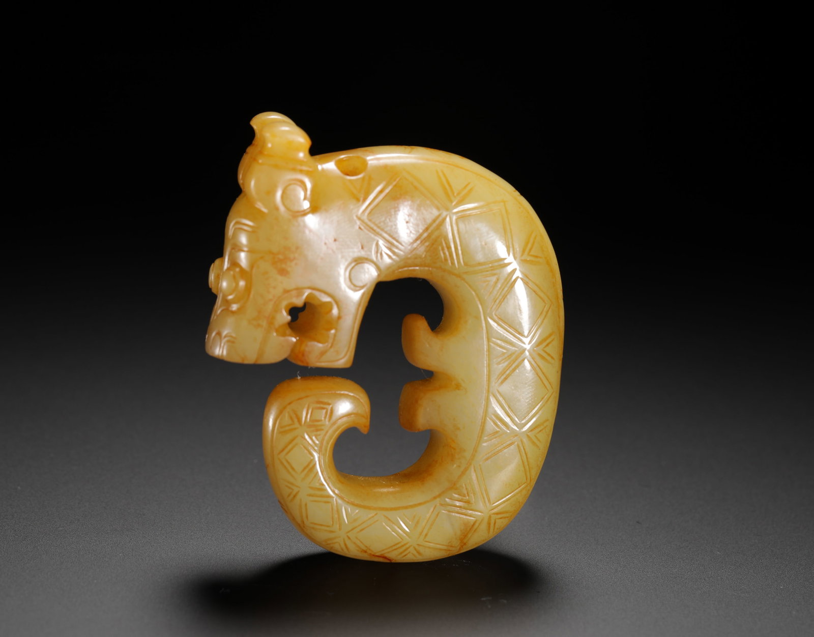 HAN DYNASTY YELLOW JADE C-SHAPED DRAGON PENDANT: H:7.2cm(2.83in)W:5.5cm(2.17in)Weight:100g(0.22lb)This is a Han Dynasty yellow jade C-shaped dragon pendant decorated with grid patterns, with a simple and ancient form. Worn by the nobility, it reflec