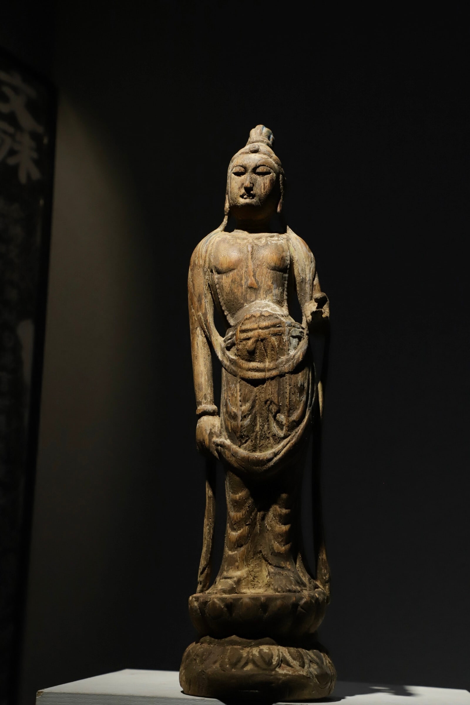 A STANDING WOODCARVING OF GUANYIN BODHISATTVA FROM THE SONG DYNASTY: H:55cmThis is an ancient wooden-carved standing statue of Guanyin Bodhisattva, carved from wood. Guanyin stands upright with a serene expression, atop a lotus pedestal. It is a simple and elegant