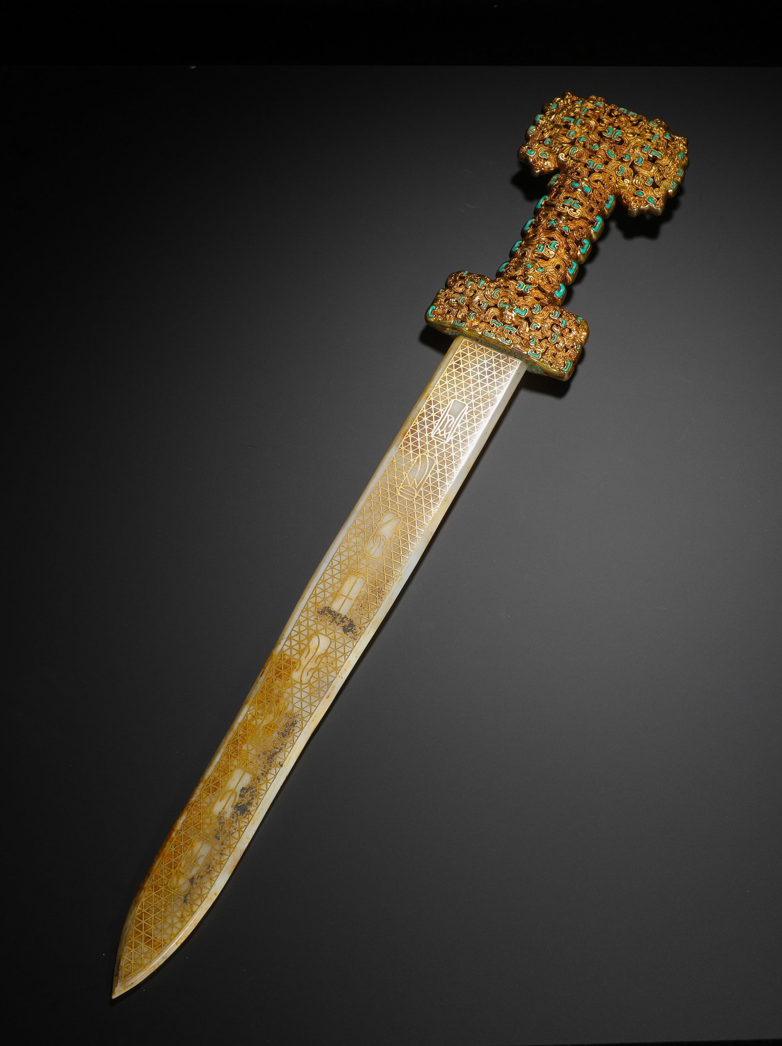 A GILDED BRONZE SWORD INLAID WITH PINE AND JADE FROM THE HAN DYNASTY: H:58cmW:9cmWeight:1010g This is a jade sword with a gold-gilded and turquoise-inlaid bronze hilt from the Han Dynasty, its blade decorated with gold-inlay technique, representing a high-status ritual 