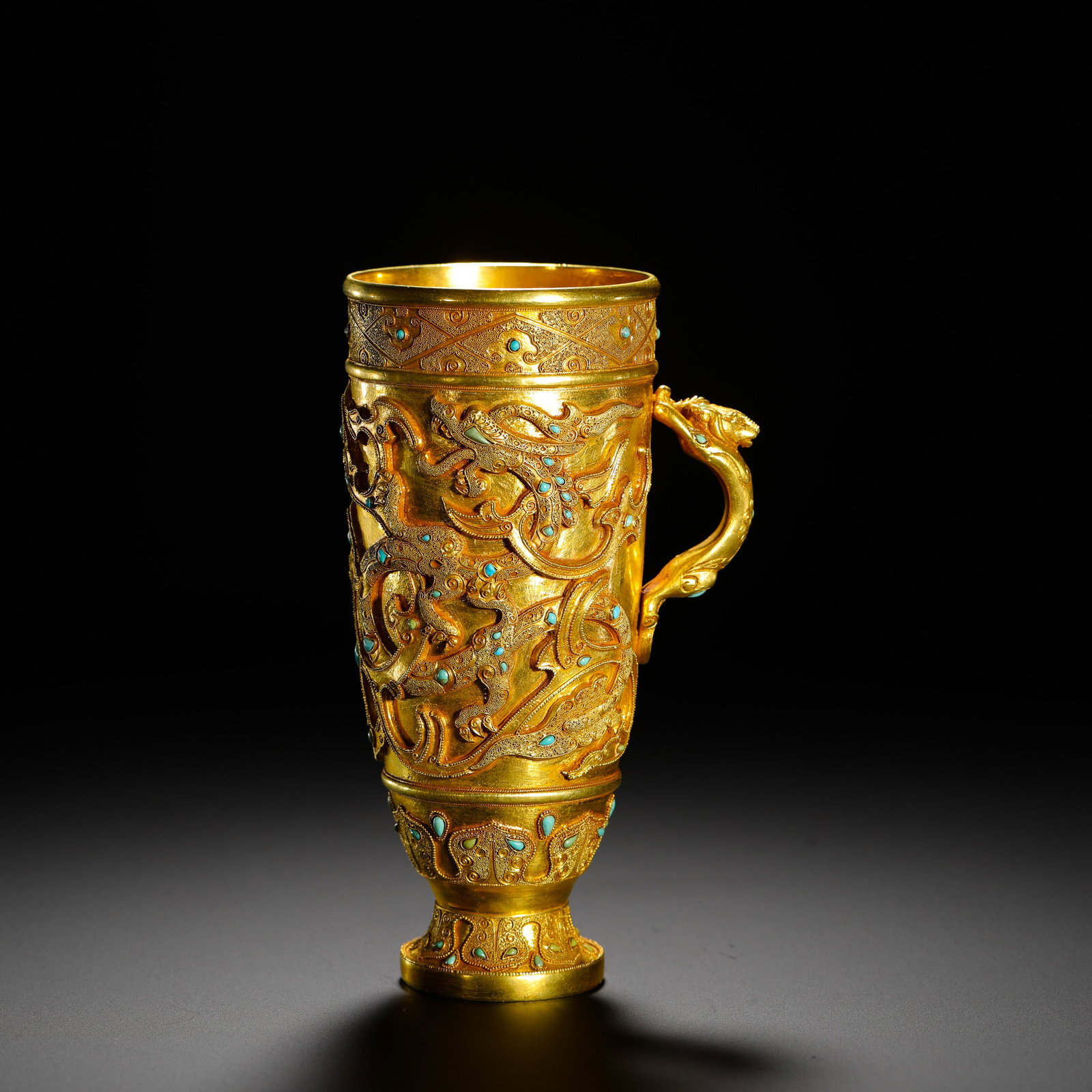 TANG SILVER GILT WITH TURQUOISE DRAGON PATTERN SINGLE-EARED HIGH-FOOTED CUP: HEIGHT:15CM (5.91IN) WIDTH:9CM (3.54IN) WEIGHT:460G (1.01LB) GILT SILVER STEMMED CUP WITH SINGLE HANDLE INLAID WITH TURQUOISE, TANG DYNASTY. THE BODY IS DECORATED WITH HIGH-RELIEF DOUBLE DRAGONS, TURQ