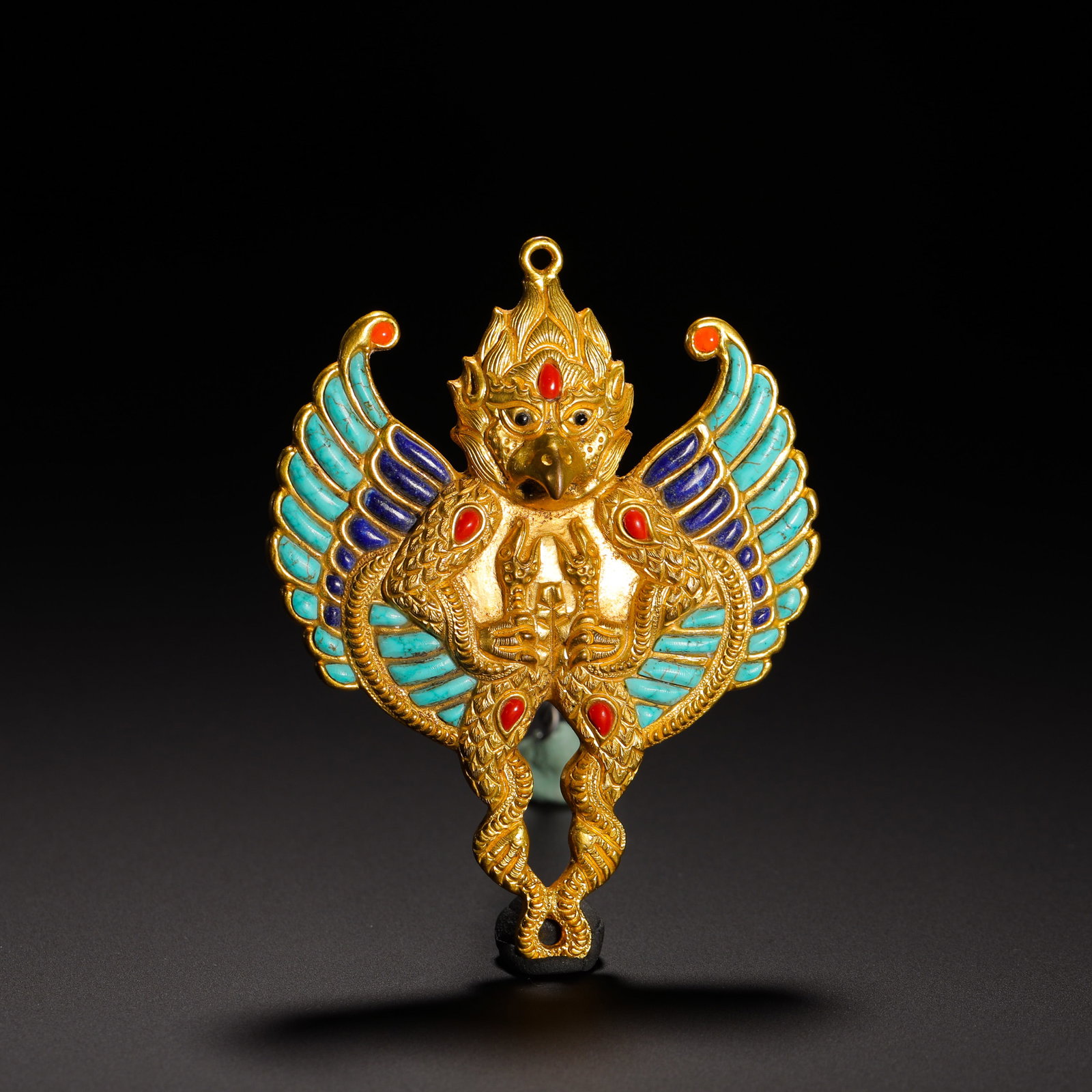 QING DYNASTY GILDED BRONZE GARUDA PENDANT: HEIGHT:8.5CM (3.35IN) WIDTH:6.5CM (2.56IN) WEIGHT:90G (0.20LB) GILT BRONZE PENDANT OF GARUDA INLAID WITH TURQUOISE AND LAPIS LAZULI, QING DYNASTY. MODELED AFTER GARUDA, THE GOLDEN-WINGED BIRD IN TIBET
