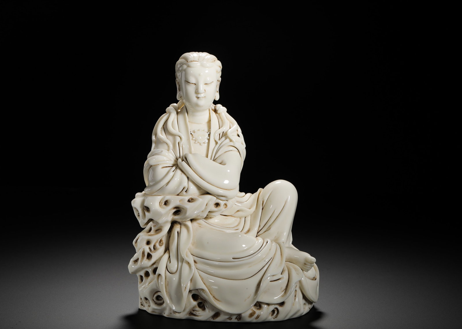 QING DYNASTY DEHUA WHITE PORCELAIN SEATED STATUE OF FREE GUANYIN: HEIGHT:20CM (7.87IN) WIDTH:13CM (5.12IN) WEIGHT:1510G (3.33LB) IVORY-WHITE DEHUA PORCELAIN GUANYIN STATUE, QING DYNASTY. FINE COMPACT BODY COVERED IN CREAMY LARD-WHITE GLAZE WITH SMOOTH JADE-LIKE LUST
