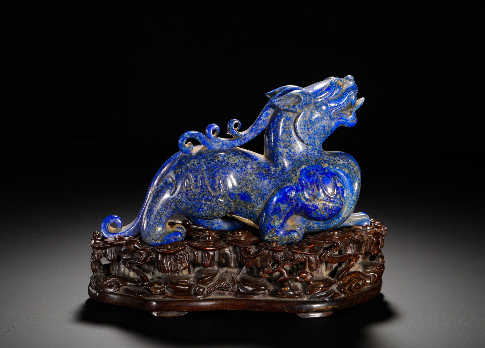 QING DYNASTY LAPIS LAZULI AUSPICIOUS BEAST PI XIU: HEIGHT:14CM (5.51IN) WIDTH:18CM (7.09IN) WEIGHT:1030G (2.27LB) SOLID LAPIS LAZULI CARVED PIXIU ORNAMENT, QING DYNASTY, MATCHED WITH HOLLOW CARVED RED SANDALWOOD BASE. CARVED FROM ONE WHOLE NATURAL LAP