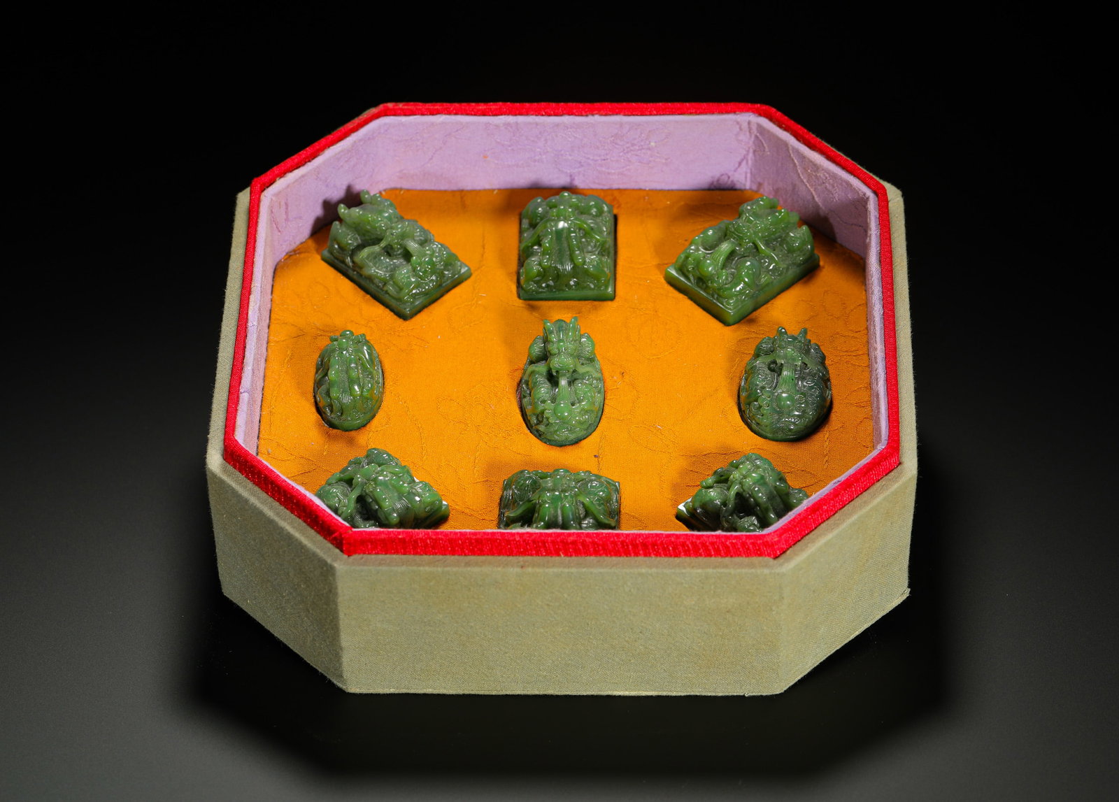 A SET OF NINE TREASURES OF HETIAN JADE SEAL FROM THE QING DYNASTY: H:2.8CMW:4CMSET OF NINE QING DYNASTY HETIAN SPINACH JADE IMPERIAL SEALS, EACH CARVED WITH INTERTWINED DRAGON KNOBS IN SQUARE AND OVAL FORMS, HOUSED IN AN ORIGINAL OCTAGONAL SILK-LINED BOX WITH GOLDEN-