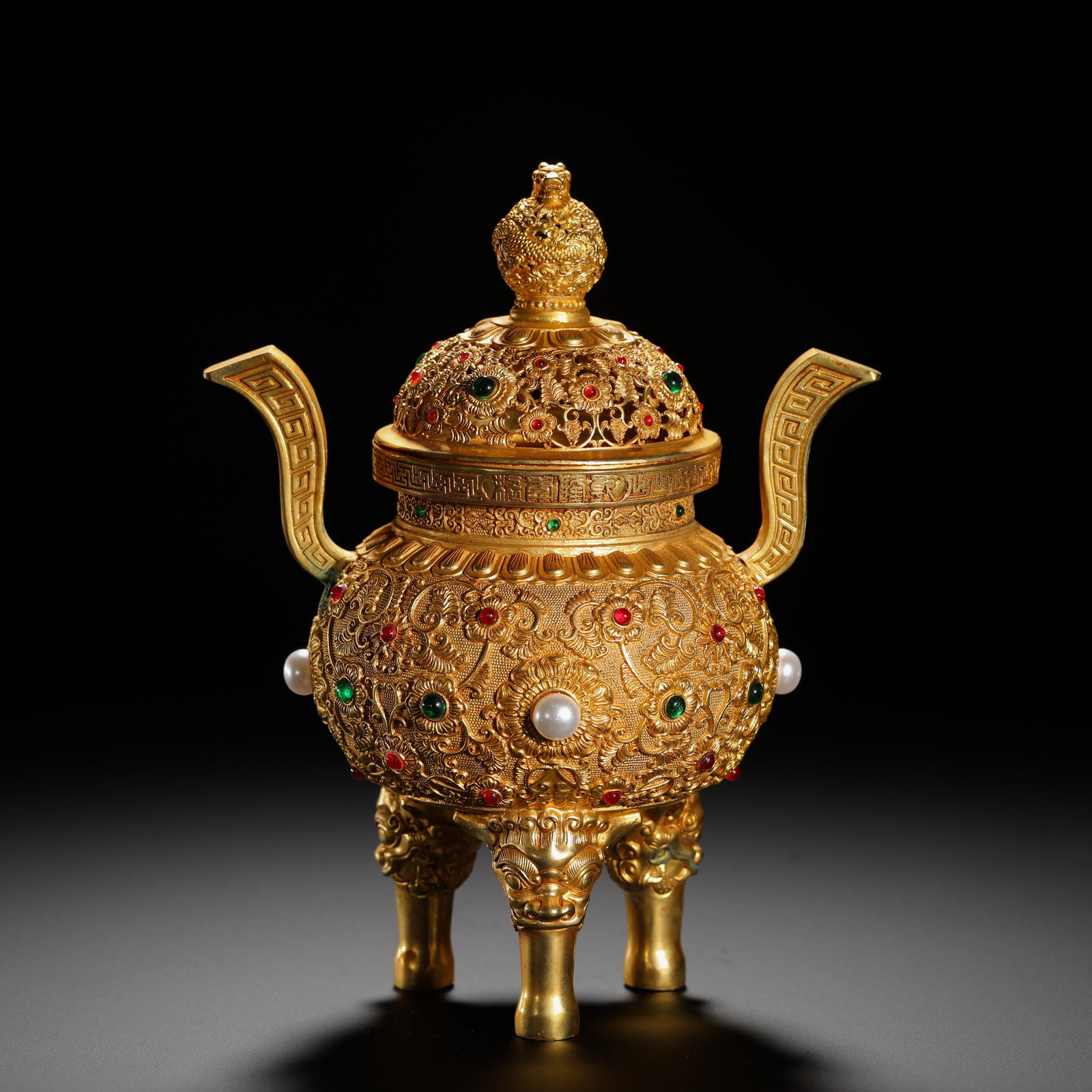 A GILDED BRONZE INCENSE BURNER WITH ENGRAVED LOTUS BRANCHES AND INLAID TREASURES FACING THE CROWN: HEIGHT:15.5CM (6.10IN) WIDTH:19CM (7.48IN) WEIGHT:600G (1.32LB) GILT BRONZE CENSER WITH BEAST FEET AND UPTURNED HANDLES, QING DYNASTY. THE WHOLE BODY IS CHASED WITH INTERLOCKING LOTUS SCROLLS. THE PIE
