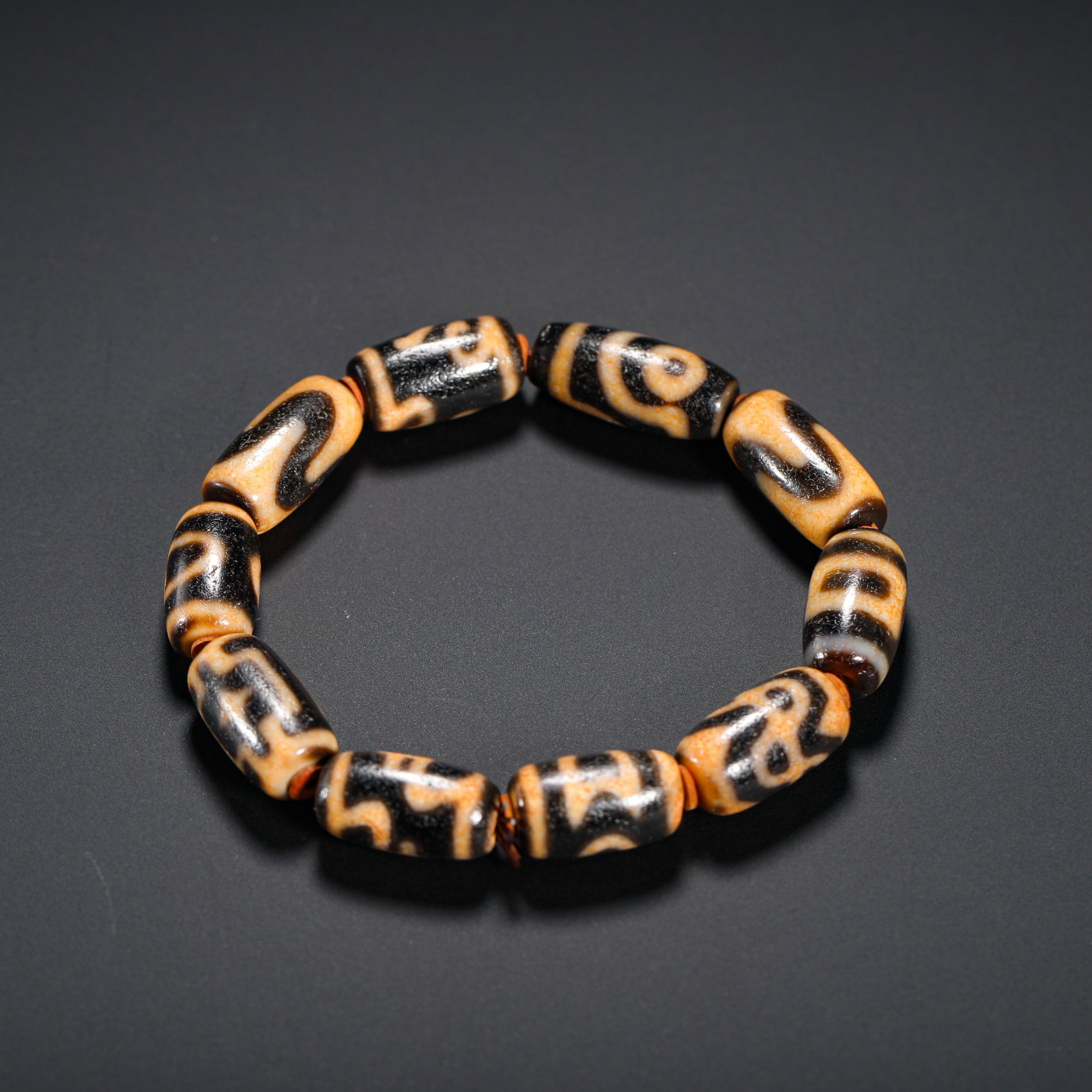 TANG DYNASTY MULTI-TOTEM OLD BEAD BRACELET: DIAMETER:1.9CM (0.75IN) WEIGHT:40G (0.09LB) BRACELET COMPOSED OF ANTIQUE DZI BEADS WITH MULTIPLE TOTEMS. TEN BARREL-SHAPED DZI BEADS FEATURE VARIOUS SACRED PATTERNS: VASE, TIGER TOOTH, TWO EYES, WATER
