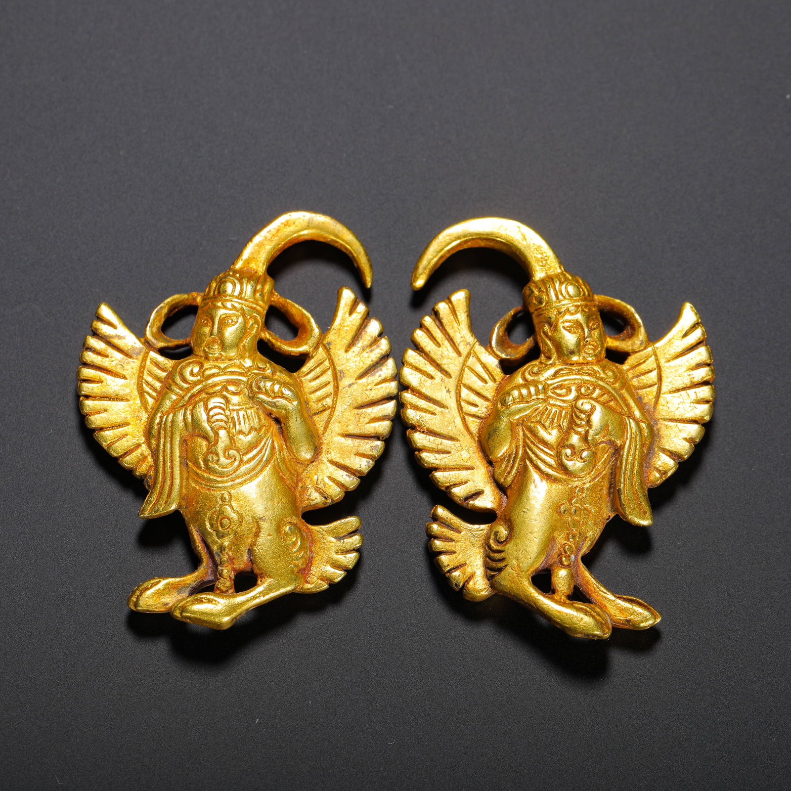 A PAIR OF GILDED BRONZE GARUDA EARRINGS FROM THE LIAO DYNASTY: HEIGHT:5.1CM (2.01IN) WIDTH:3.6CM (1.42IN) WEIGHT:60G (0.13LB) PAIR OF BRONZE-GILDED GARUDA EARRINGS, LIAO-JIN DYNASTIES. CRAFTED WITH COMBINED HAMMERING AND CHASING TECHNIQUES, COVERED IN THICK GENUI