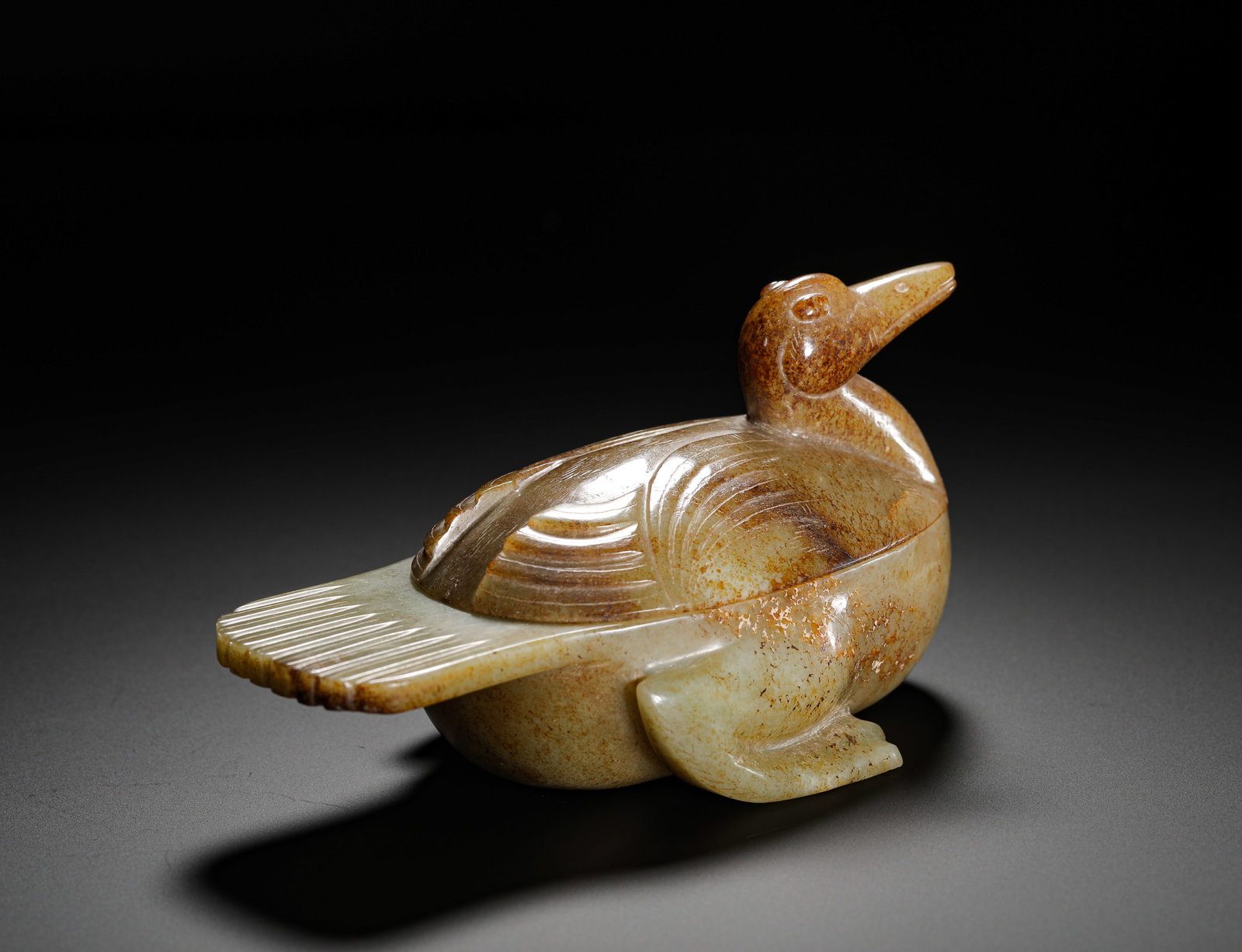 TANG DYNASTY HETIAN JADE RED-SOAKED MANDARIN DUCK SHAPED LID BOX: HEIGHT:8CM (3.15IN) WIDTH:24.5CM (9.65IN) WEIGHT:260G (0.57LB) ARCHAIC CELADON JADE MANDARIN DUCK LIDDED BOX WITH RUSSET PATINA.SEPARATELY CARVED BODY AND LID FROM ONE JADE MASS, FULLY COVERED IN AGED