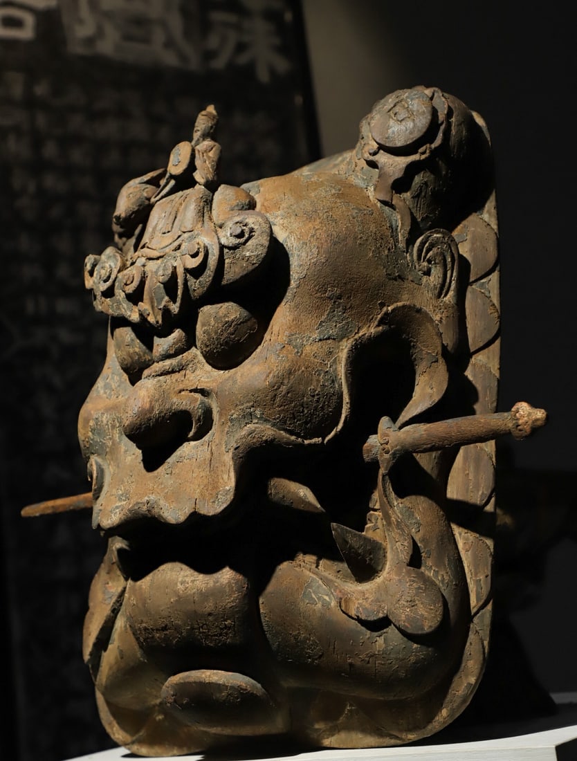 MING DYNASTY NANMU MOUTH: H: 43CM L: 33CM T: 16CM, L: 45CMTHIS IS AN ANCIENT WOODEN-CARVED FANGXIANG MASK (OR TOMB-GUARDING TALISMAN) CARVED FROM A SINGLE PIECE OF WOOD, IT HAS A FIERCE AND MAJESTIC APPEARANCE, WITH A LONG ROD