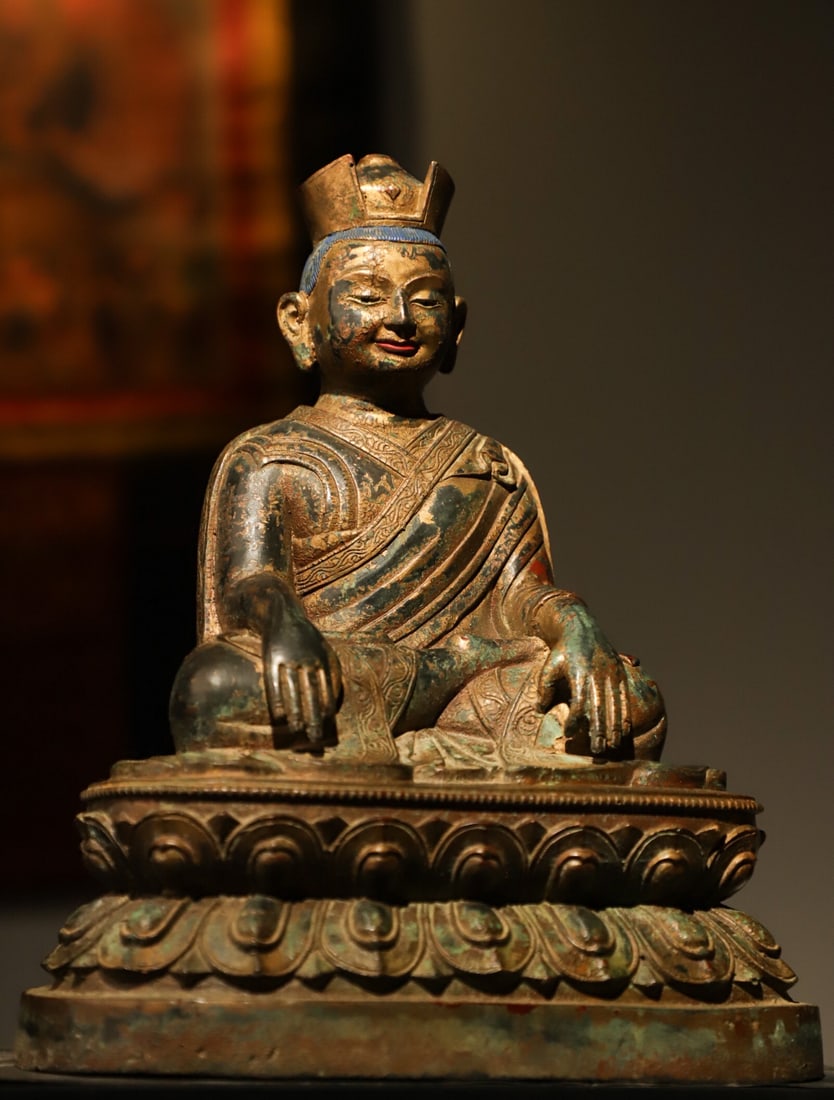 A GILDED BRONZE STATUE OF A MASTER FROM THE MING DYNASTY: H:26L:22W:16CM. WEIGHT:3700GTHIS IS A TIBETAN BUDDHIST GILT-BRONZE SITTING STATUE OF A LAMA (GURU) . MADE OF GILT BRONZE, THE LAMA WEARS A DHARMA KING??S HAT, WITH A SERENE AND COMPASSIONATE EXPRESSIO