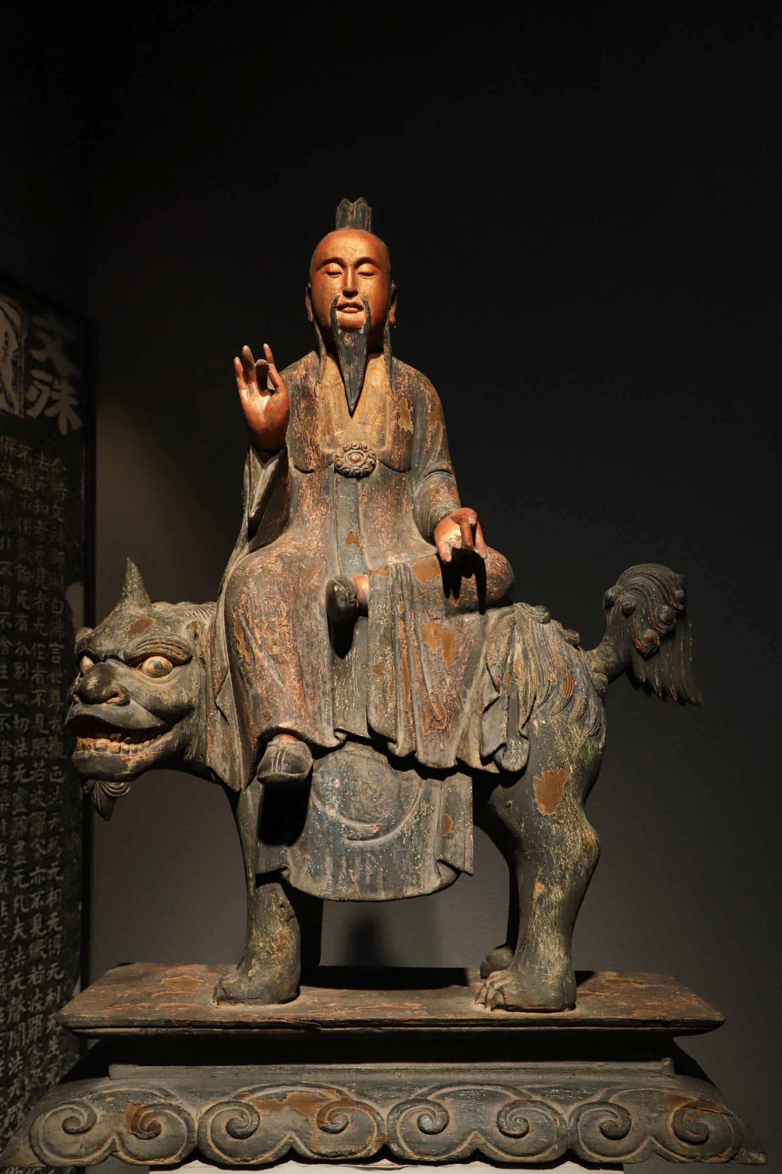 A PAINTED WOODCARVING OF THE MING DYNASTY DEPICTING THE GREAT LORD OF SALVATION RIDING A LION: H:95CM (37.40IN) L:66CM (25.98IN) W:28CM (11.02IN) SOLID WOOD CARVED TAOIST DEITY FIGURE. THE DEITY WEARS A TAOIST CROWN WITH LONG BEARD, CLAD IN LOOSE ROBES WITH MOST FADED RED AND CYAN PAINT. HE RID