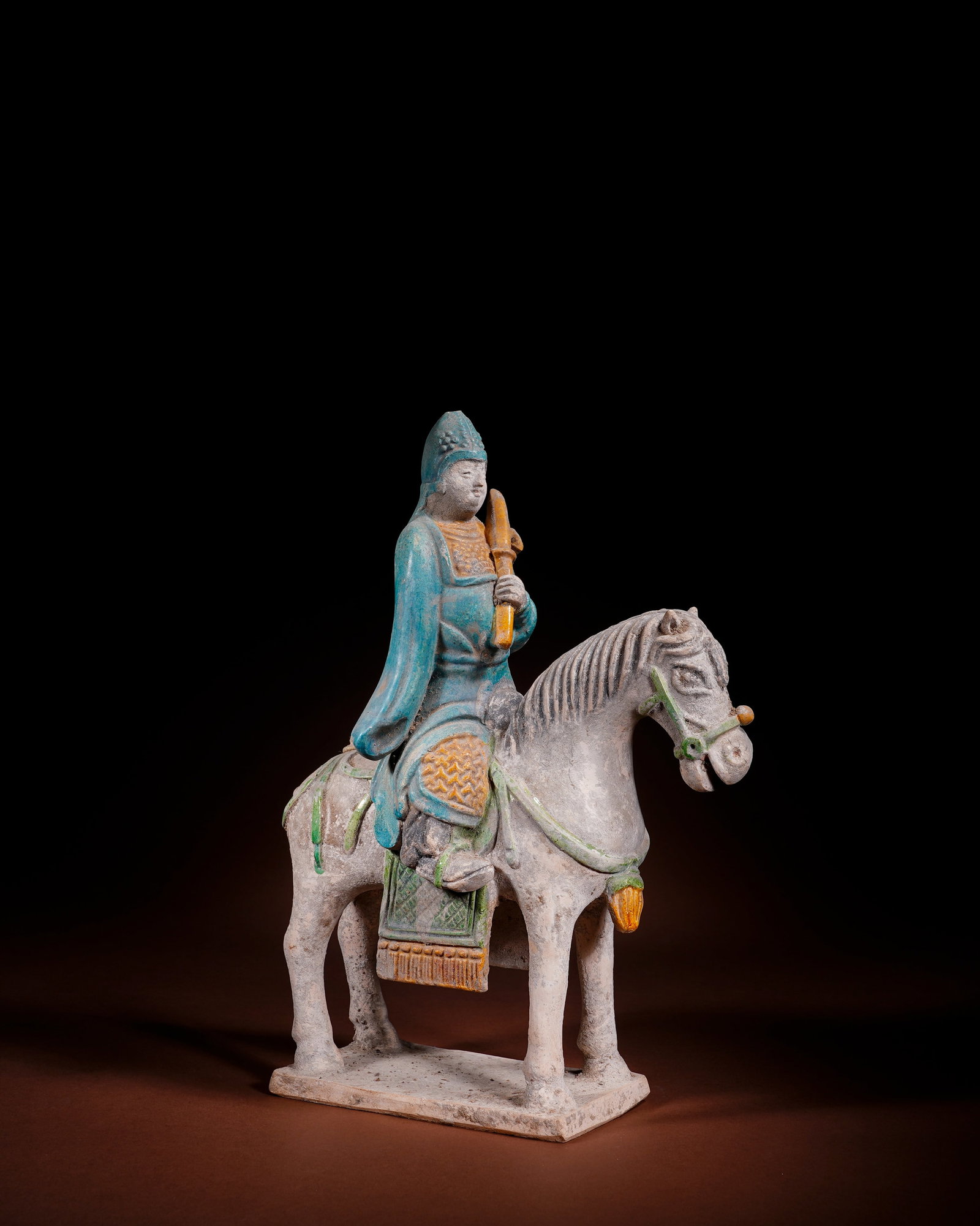 TRI-COLOR GLAZED TERRACOTTA WARRIORS OF THE MING DYNASTY: L:20cm H:29.5cm This is a low-temperature lead-glazed tri-color burial figurine of Ming Dynasty, made of white pottery body coated with green, turquoise and yellow glazes, integrated with rectangular 