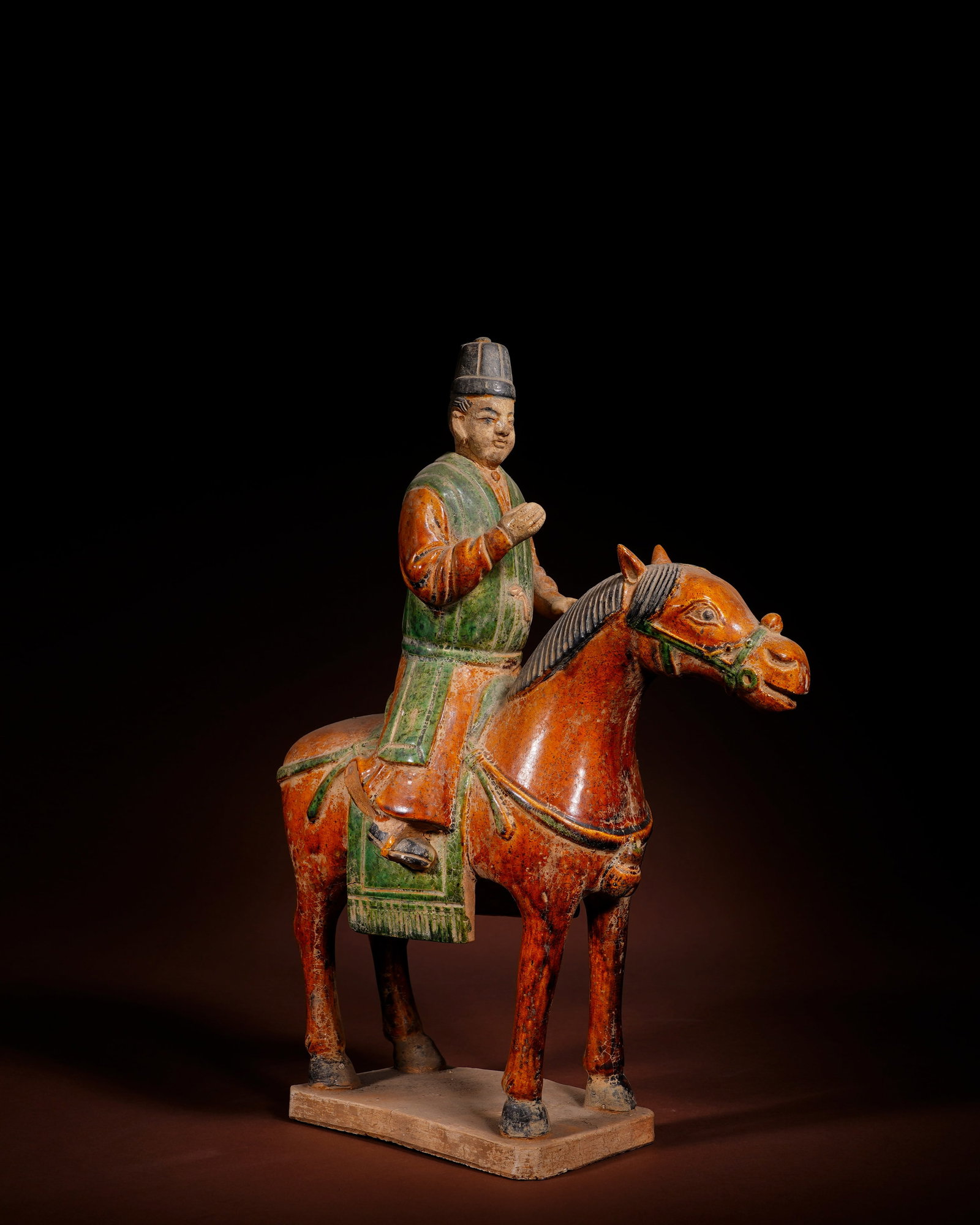 THE MING TRI-COLOR GLAZED POTTERY FIGURE OF AN OFFICIAL ON HORSEBACK WITH A GREEN BACK AND YELLOW: L:25.5cm H:34cm This low-temperature lead-glazed tri-color equestrian official figurine of Ming Dynasty is made of white clay, integrated with horse and rectangular base in one firing, covered with ye
