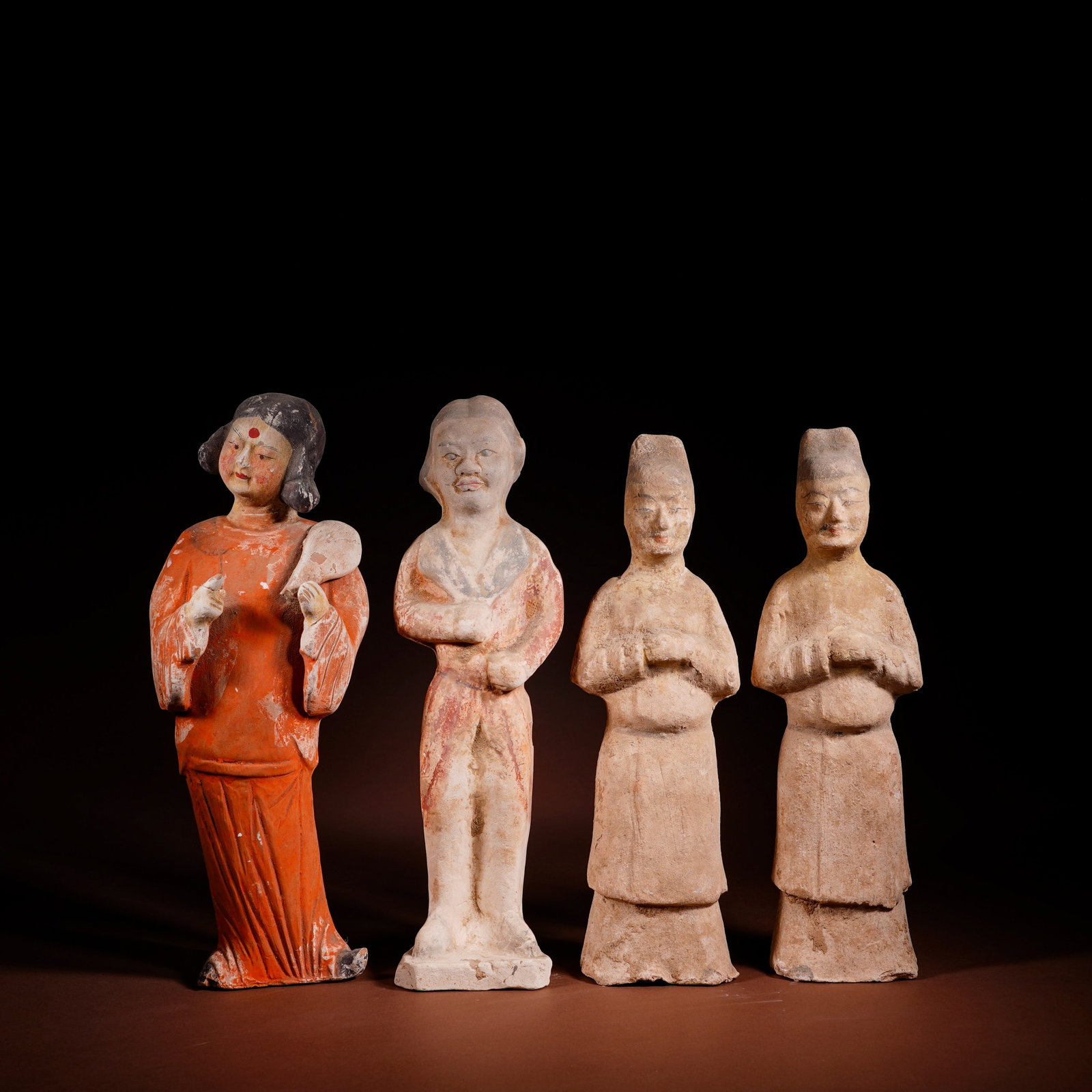 A SET OF FOUR TANG DYNASTY PAINTED MALE AND FEMALE ATTENDANTS: L:11cm H:29cm /L:8.5cm H:29cm /L:8.8cm H:27cm /L:8.6cm H:27.5cm This complete set of four painted pottery attendants of Tang Dynasty is molded from white clay, decorated with cinnabar, ink and white m